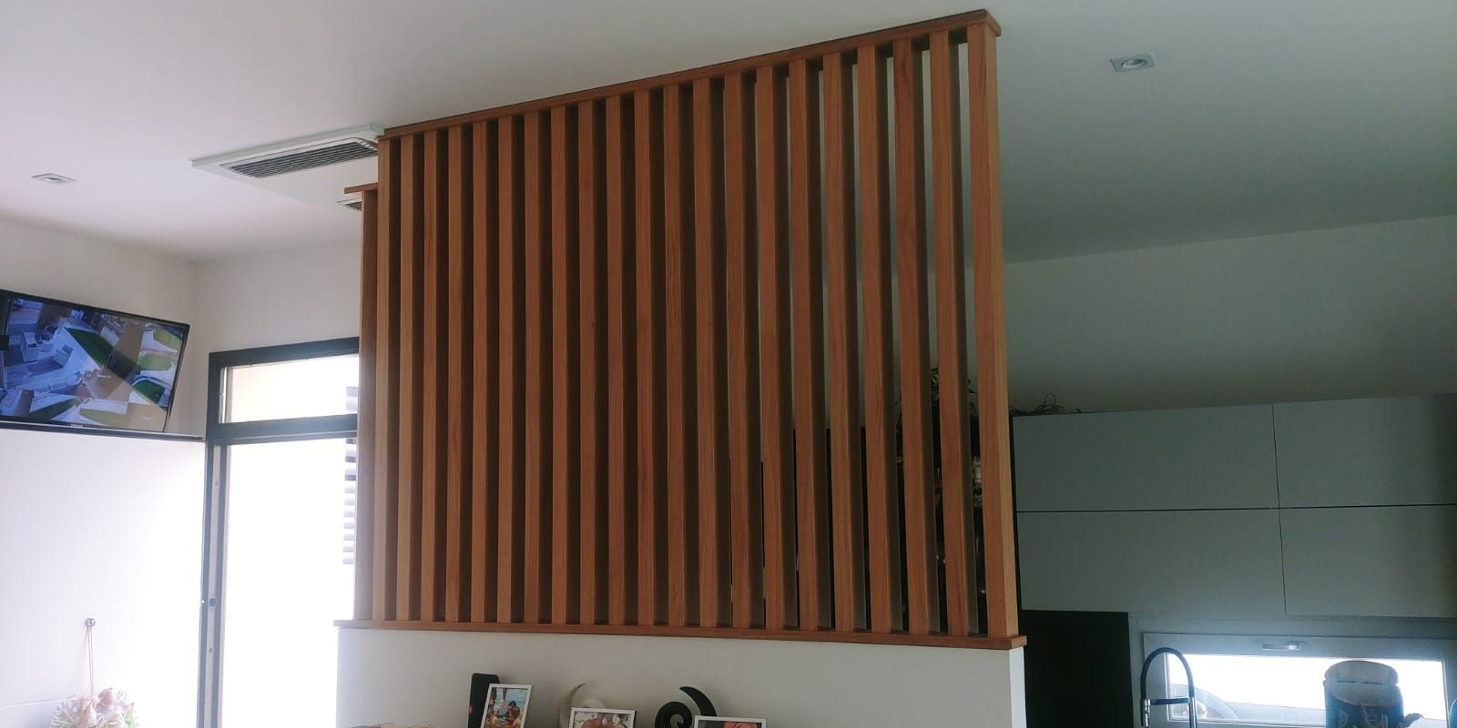 Un divisorio in doghe di legno marrone che divide due stanze di una casa. Una stanza è illuminata da una finestra.