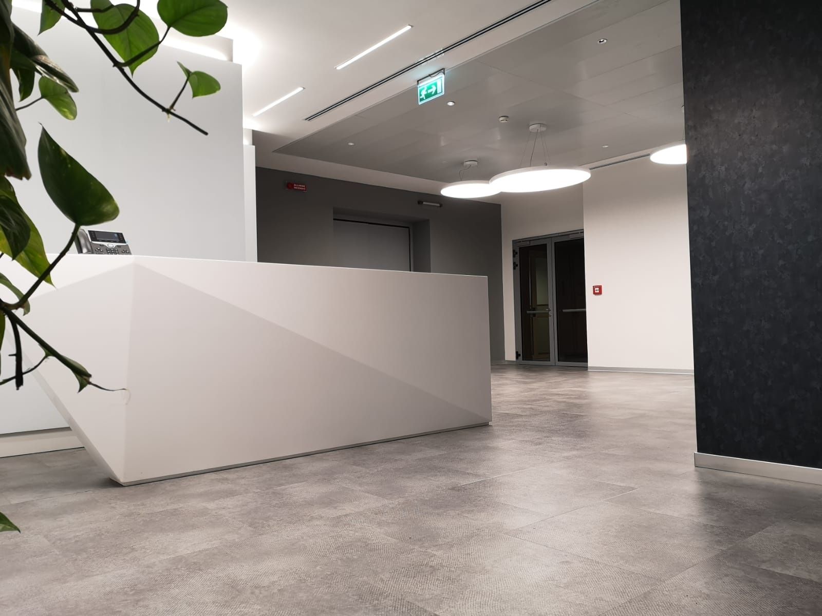 Moderna area reception per ufficio con scrivania geometrica bianca, pavimento grigio e piante.