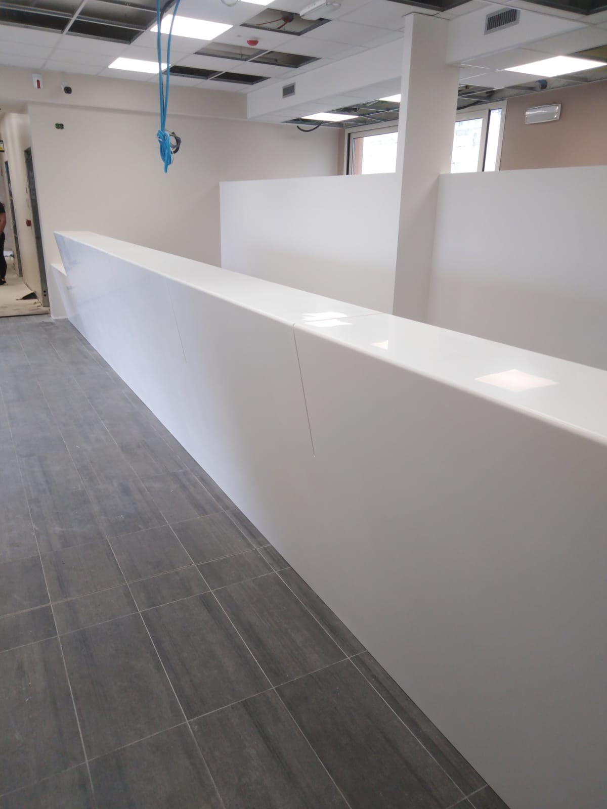 Lungo divisorio bianco in uno spazio ufficio moderno con pavimento piastrellato grigio.