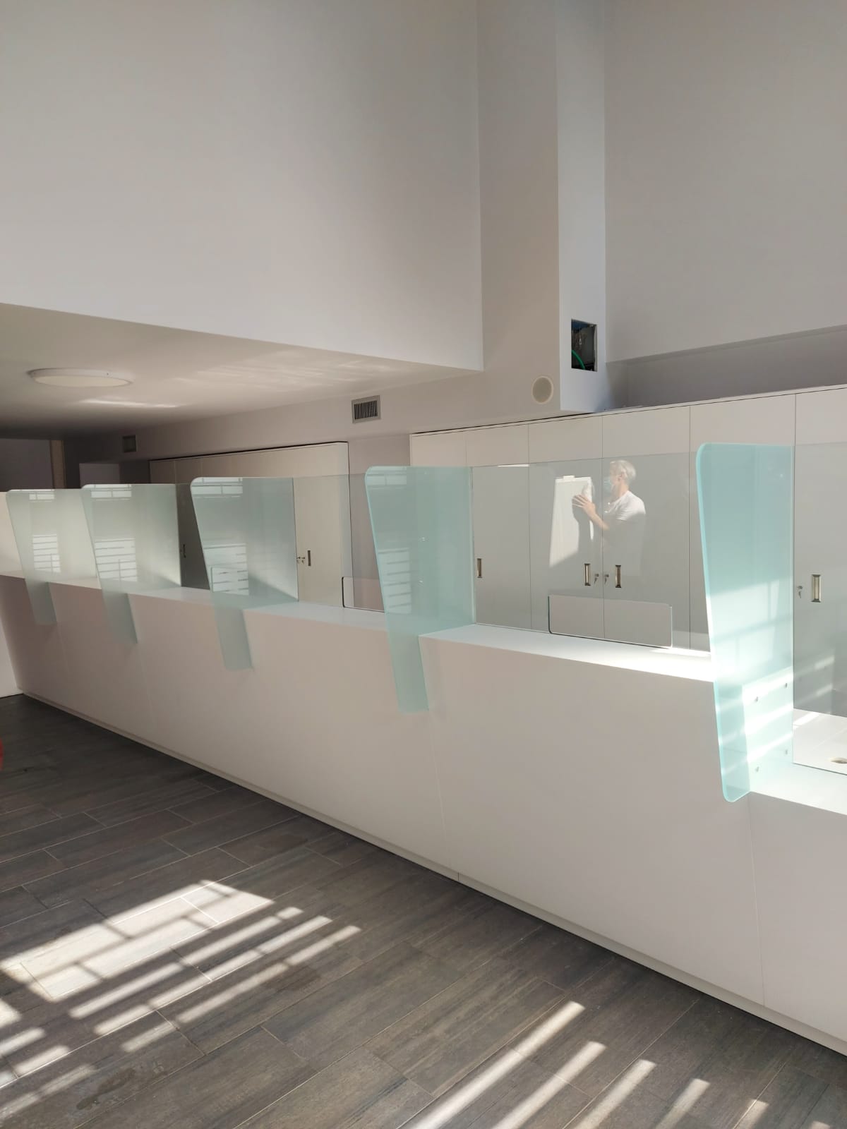 Un lungo bancone della reception bianco con divisori in vetro satinato. Uno spazio interno ben illuminato.