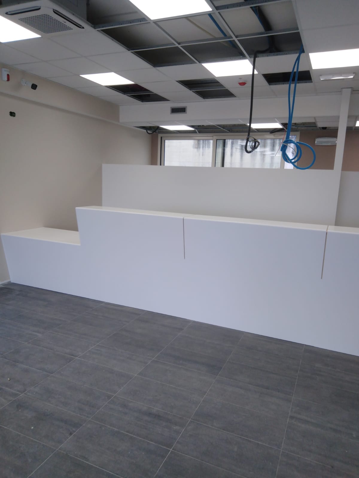 Bancone bianco a più livelli in una stanza con pavimento piastrellato grigio e soffitto a vista.