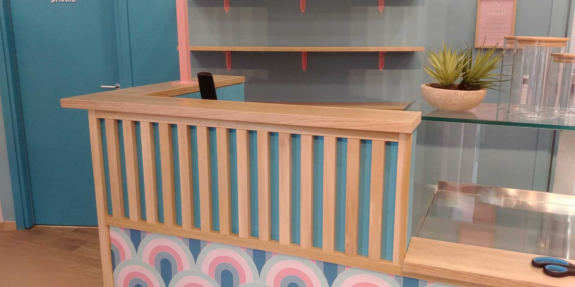 Un bancone con piano in legno e dettagli color verde acqua. Sono visibili anche mensole, piante e vetrine in vetro.