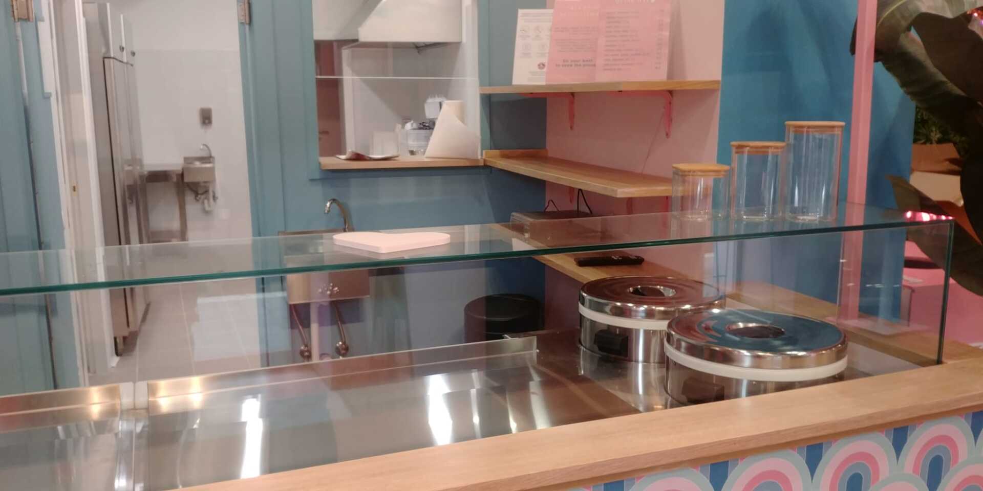 Bancone della gelateria con contenitori di metallo, barattoli di vetro e dettagli rosa e blu.