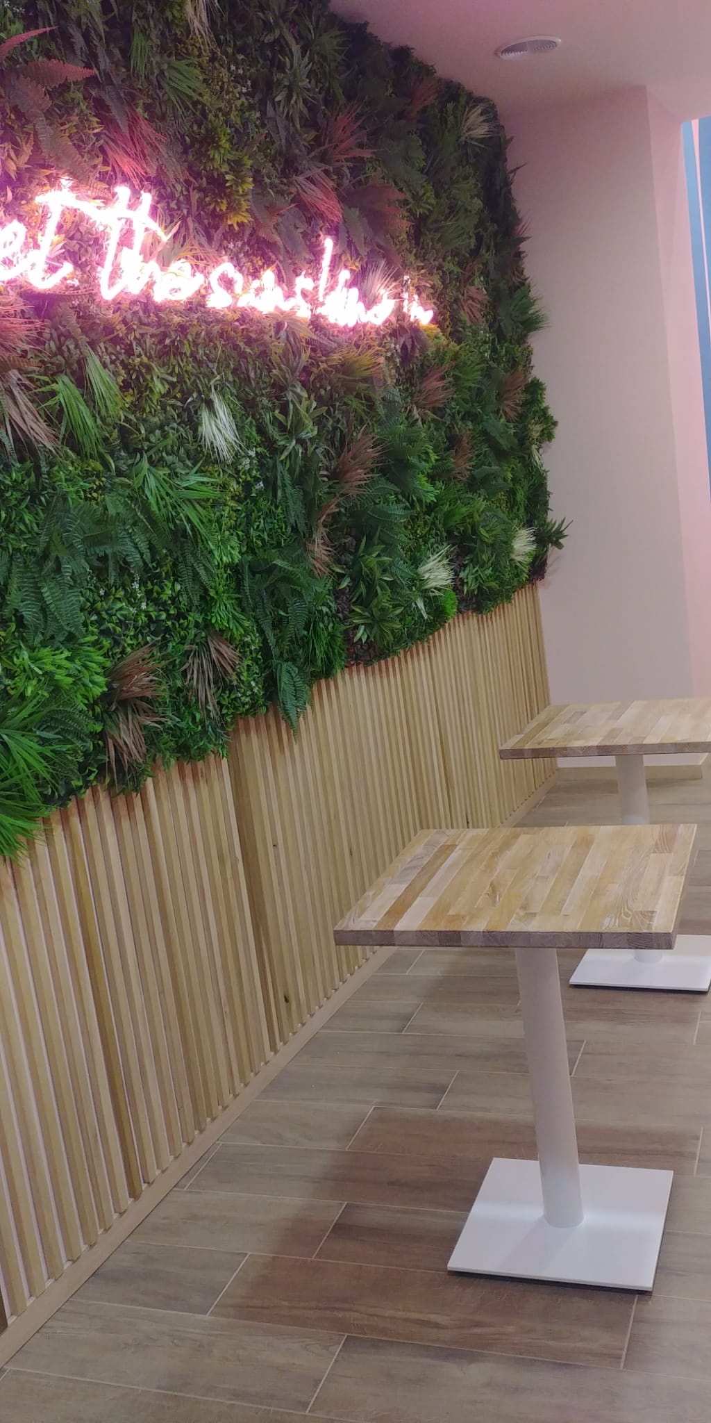 Area salotto del ristorante con tavoli quadrati, pavimenti in legno e una parete verde con insegna al neon.