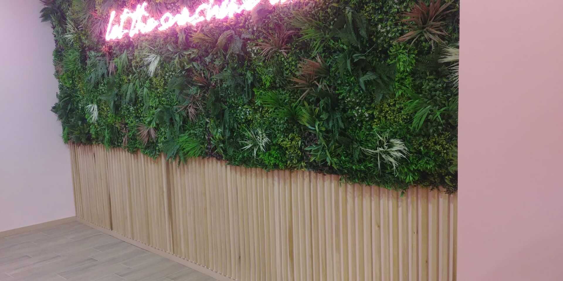 Parete con piante verdi, pannelli in legno e insegna al neon rosa, in una stanza con pareti rosa.