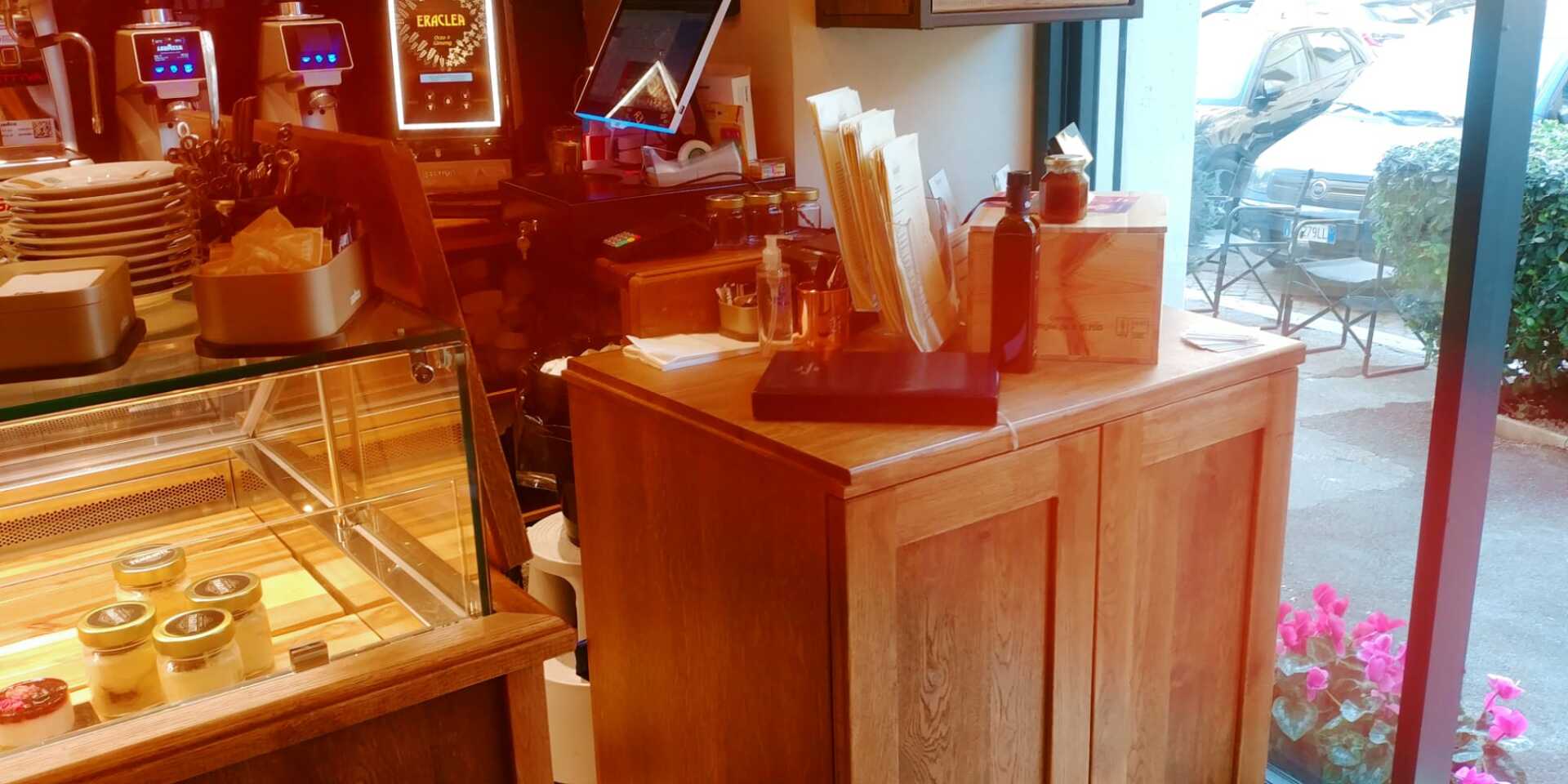 Interno di un bar, con una vetrina, armadietti in legno e una finestra che si affaccia sull'esterno.