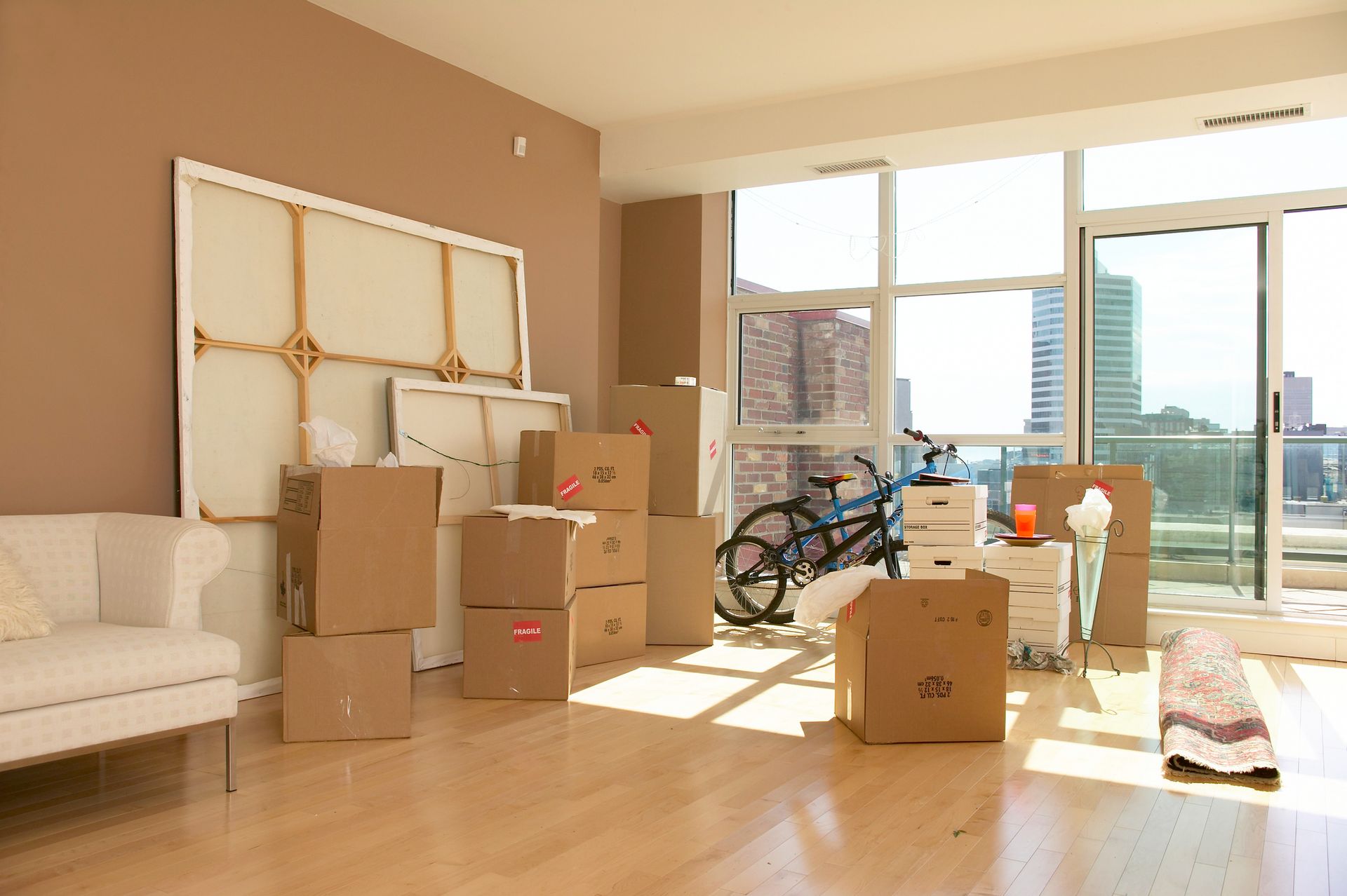 Scatoloni e oggetti personali in una stanza luminosa con un divano, opere d'arte e vista sulla città, a indicare un trasloco.