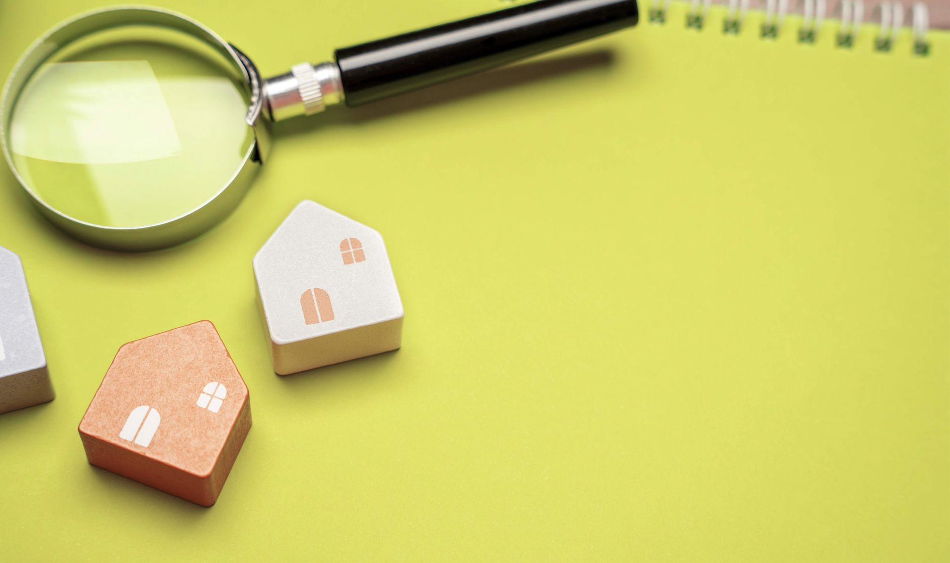 Magnifying glass and small house models on a green background with a notebook. Magnifying glass and small house models on a green background with a notebook.