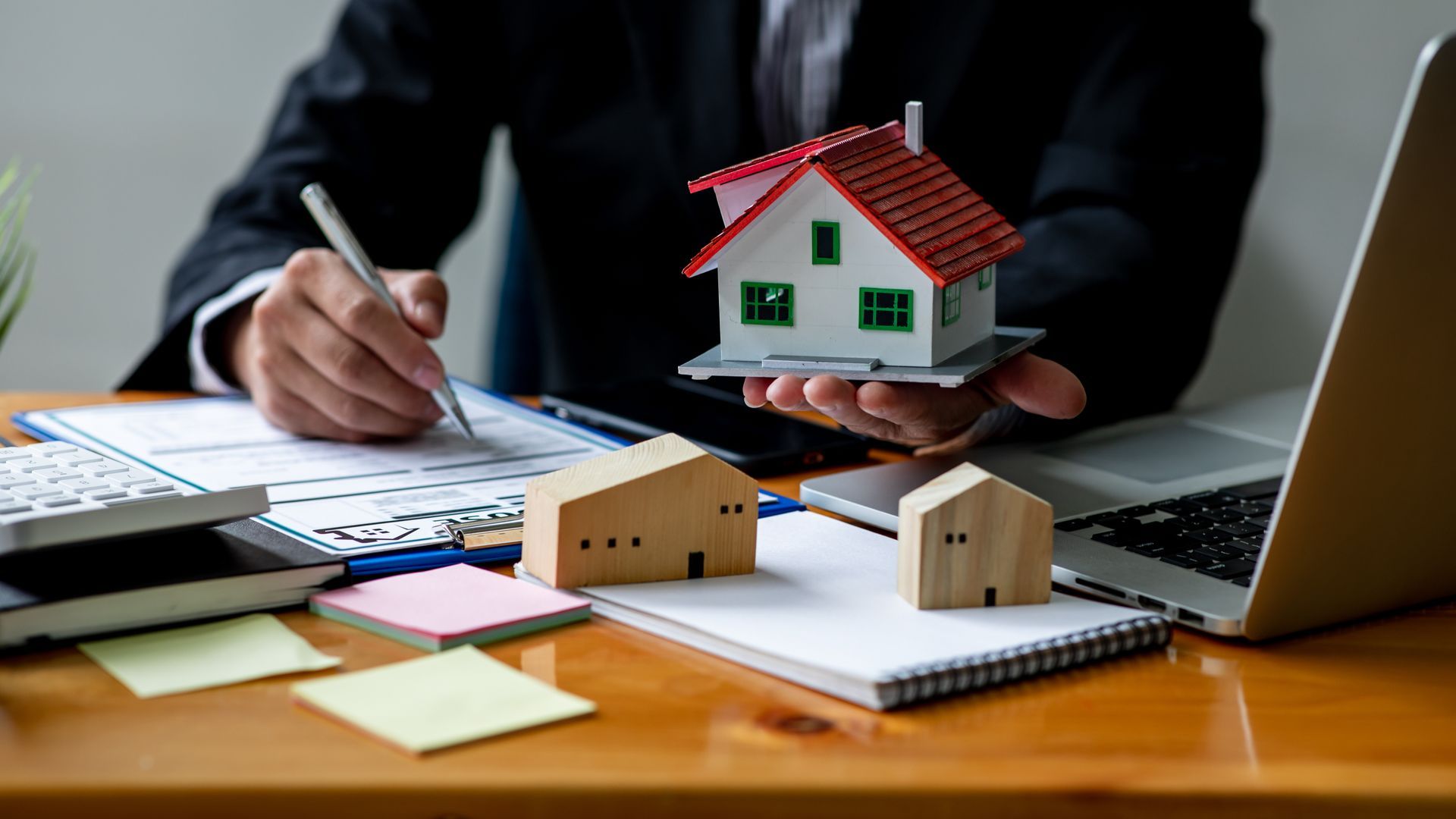 Man in suit holds a miniature house, blue background.