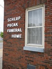 A brick building with a window and a sign on it that says schlup pucak funeral home.