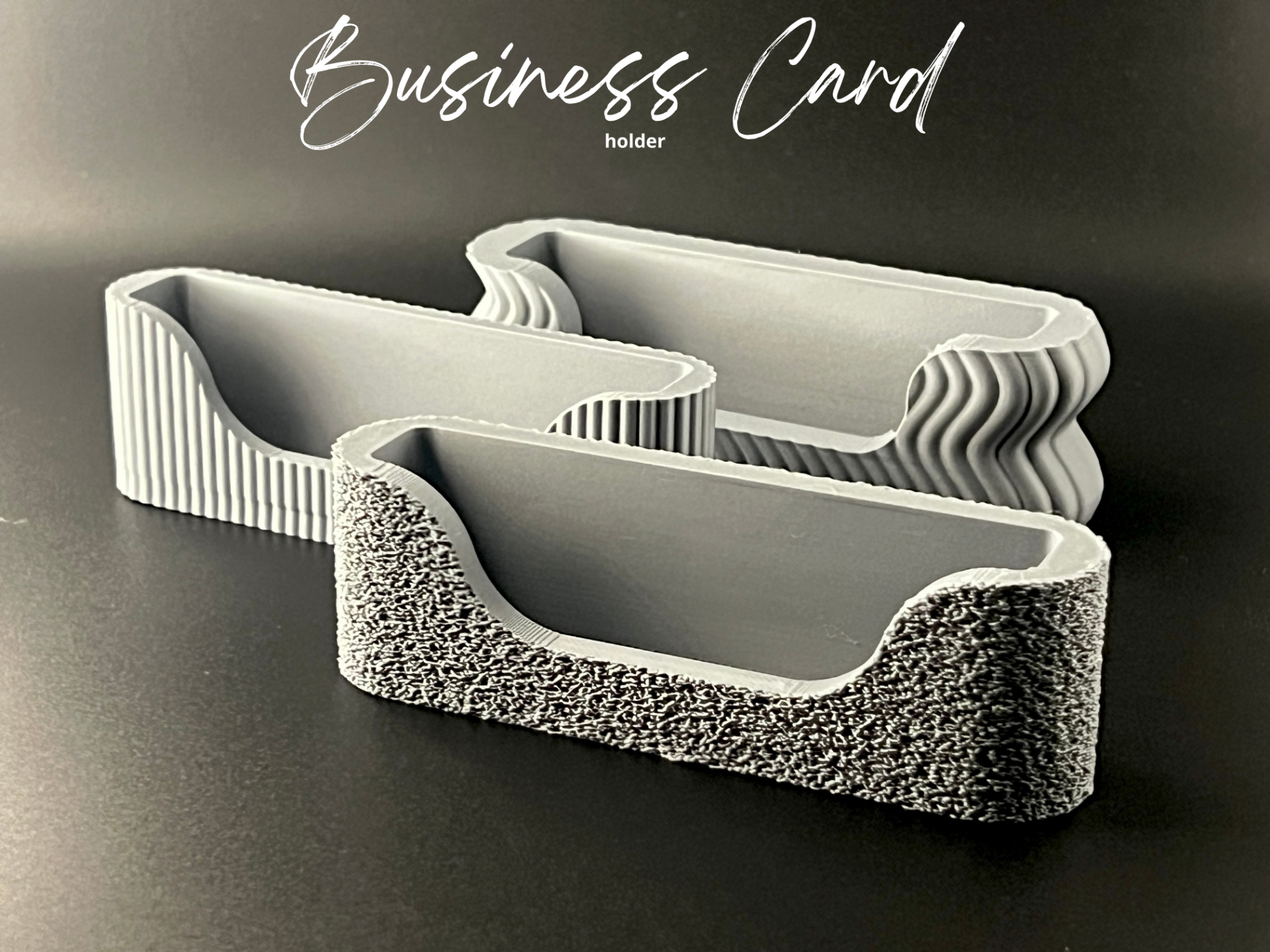 Rig-3d Drie visitekaartjeshouders van grijs beton met een gestructureerde afwerking staan op een donker oppervlak, met bovenaan het opschrift