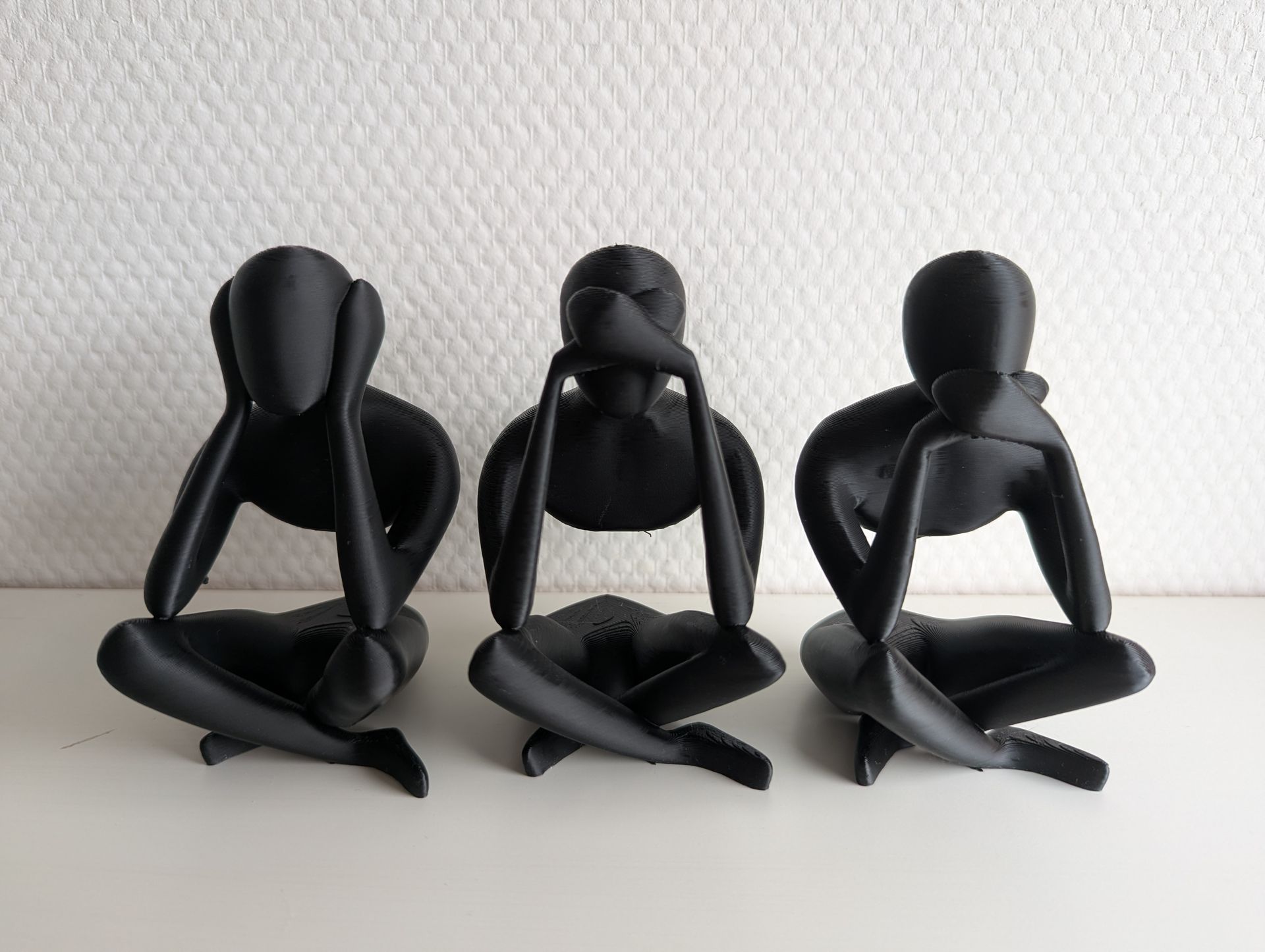 Rig-3d Drie zwarte, minimalistische mensfiguren zitten naast elkaar, elk met hun oren, mond of ogen bedekt in een peinzende houding.