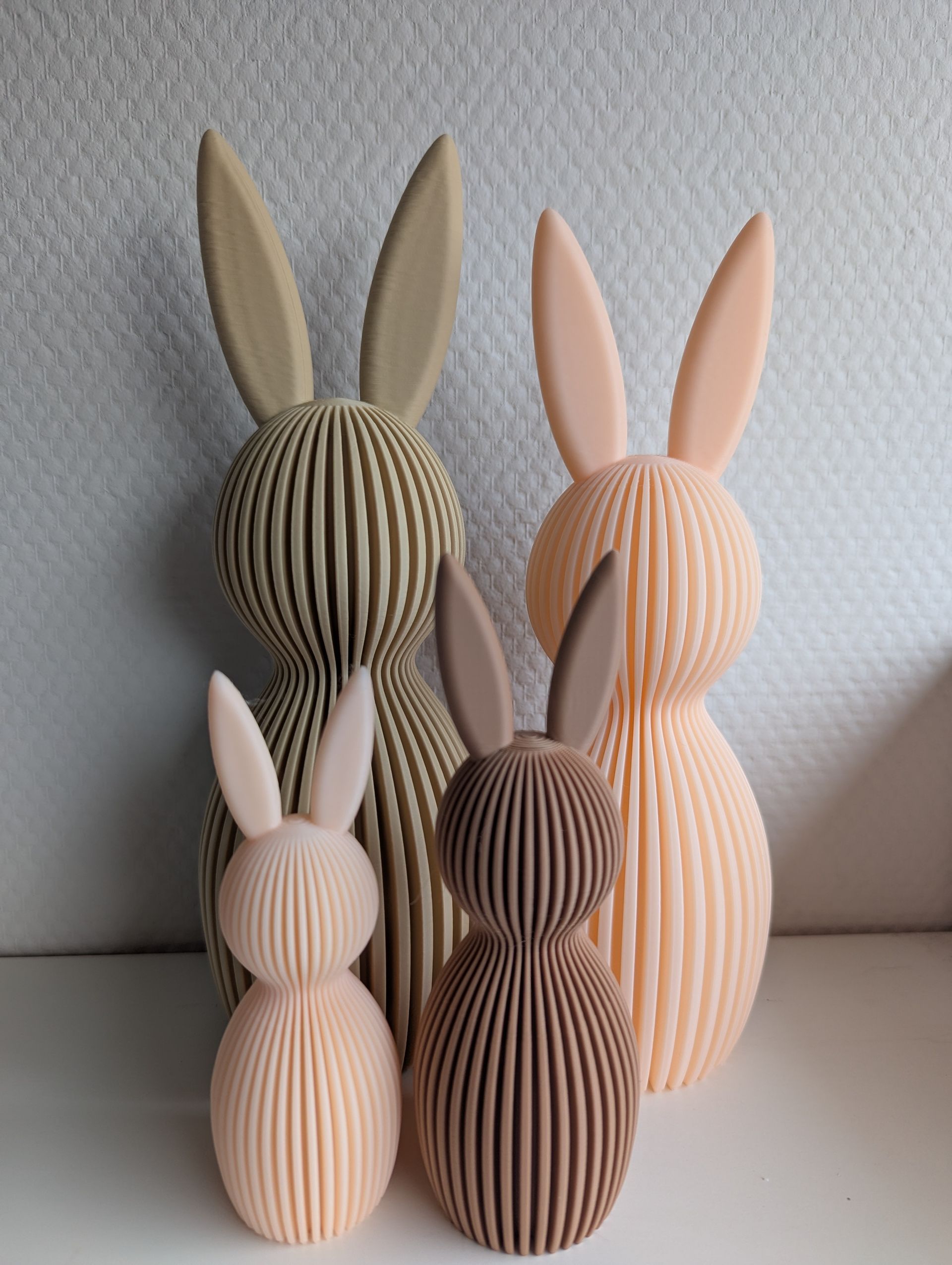 Rig-3d Vier staande konijnenbeeldjes van verschillende hoogtes en ingetogen aardetinten, met verticale ribbels als textuur.