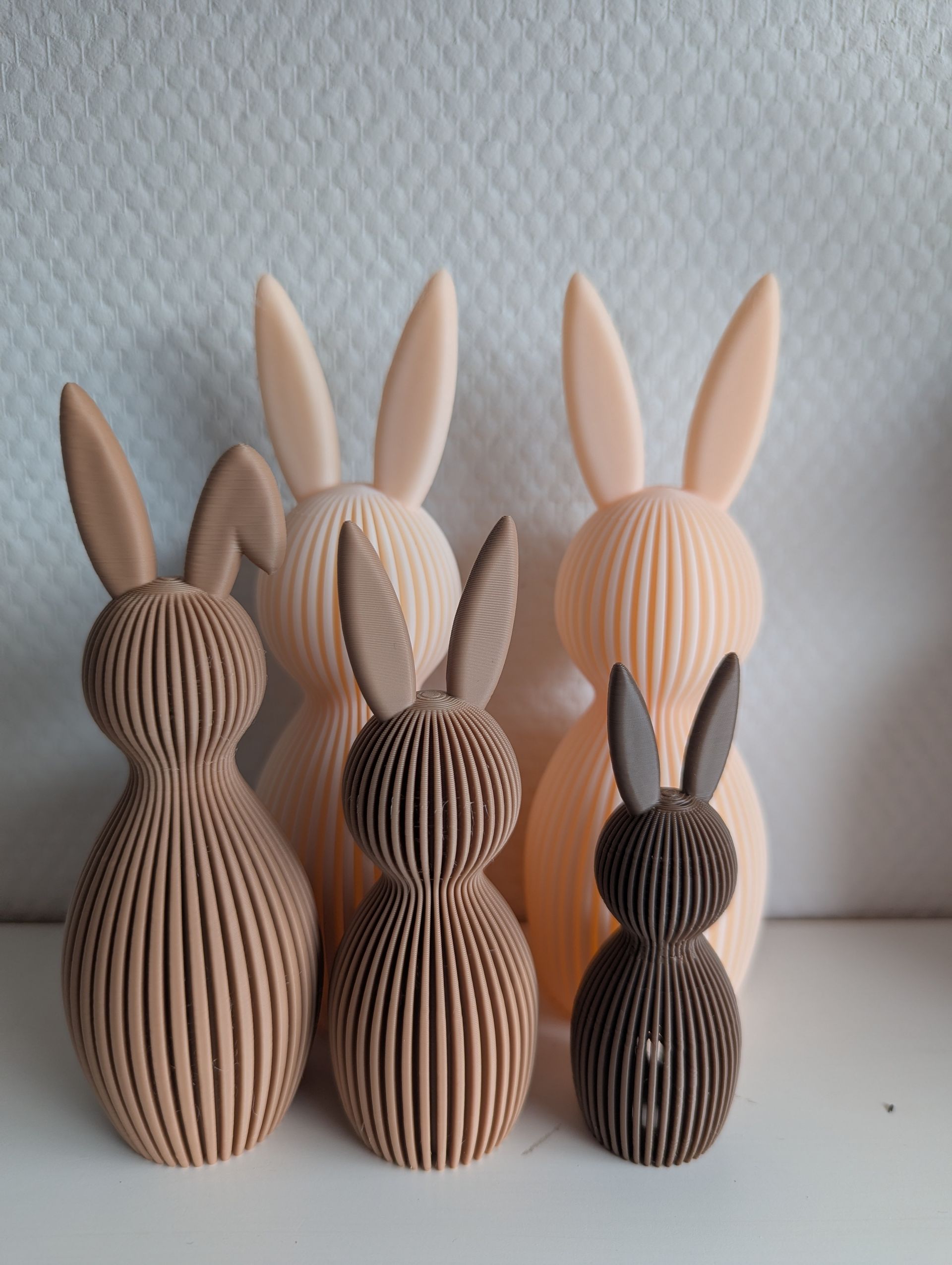 Rig-3d Een groep van vijf decoratieve, verticaal geribbelde konijnenbeeldjes in beige en bruine tinten, tentoongesteld op een witte ondergrond.