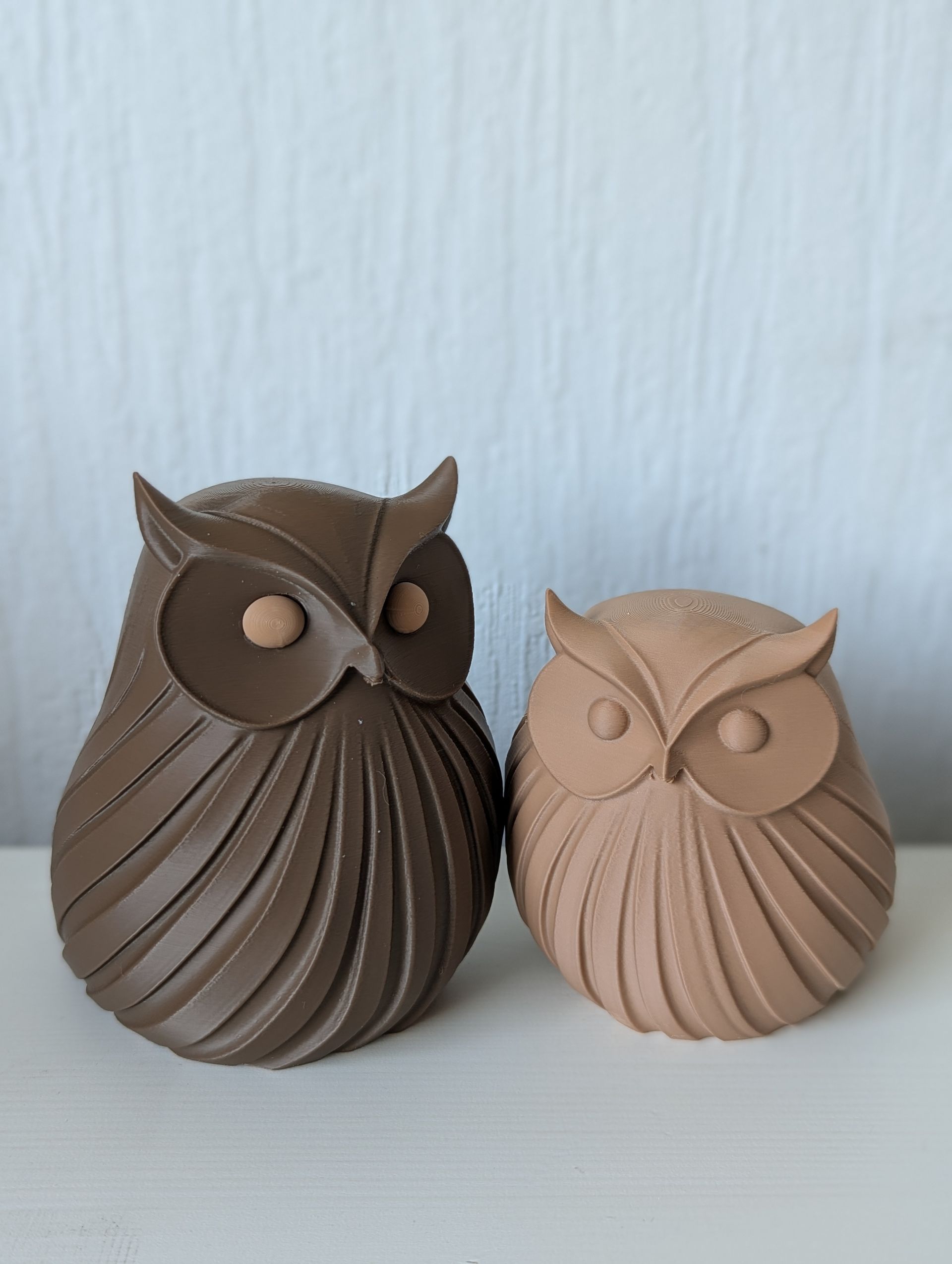 Rig-3d Twee kleine, gestileerde keramische uiltjes met een geribbeld, gestructureerd lijfje staan naast elkaar tegen een effen witte achtergrond.