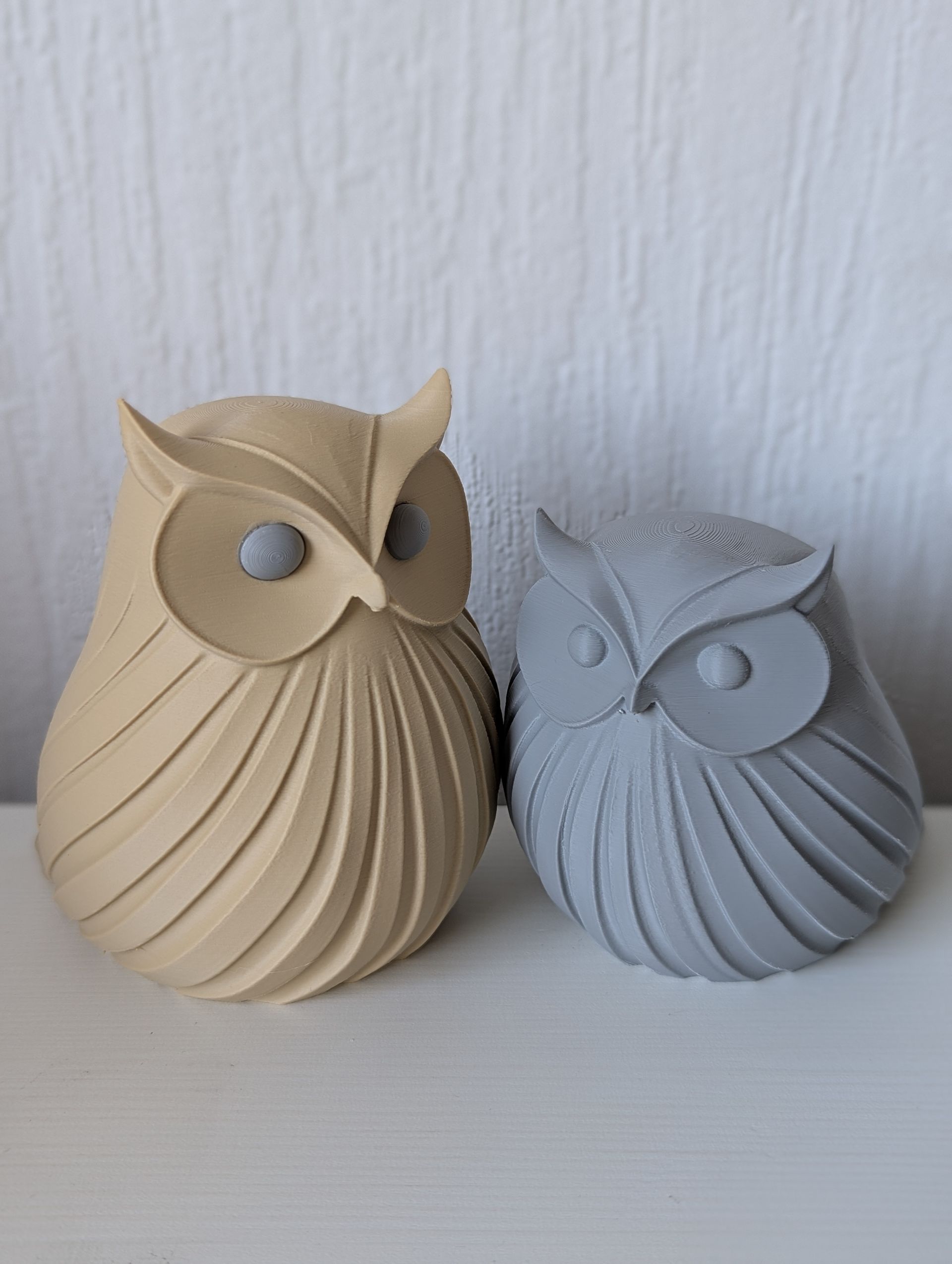 Rig-3d Twee kleine, gestileerde keramische uiltjes met een geribbeld, gestructureerd lijfje staan naast elkaar tegen een effen witte achtergrond.