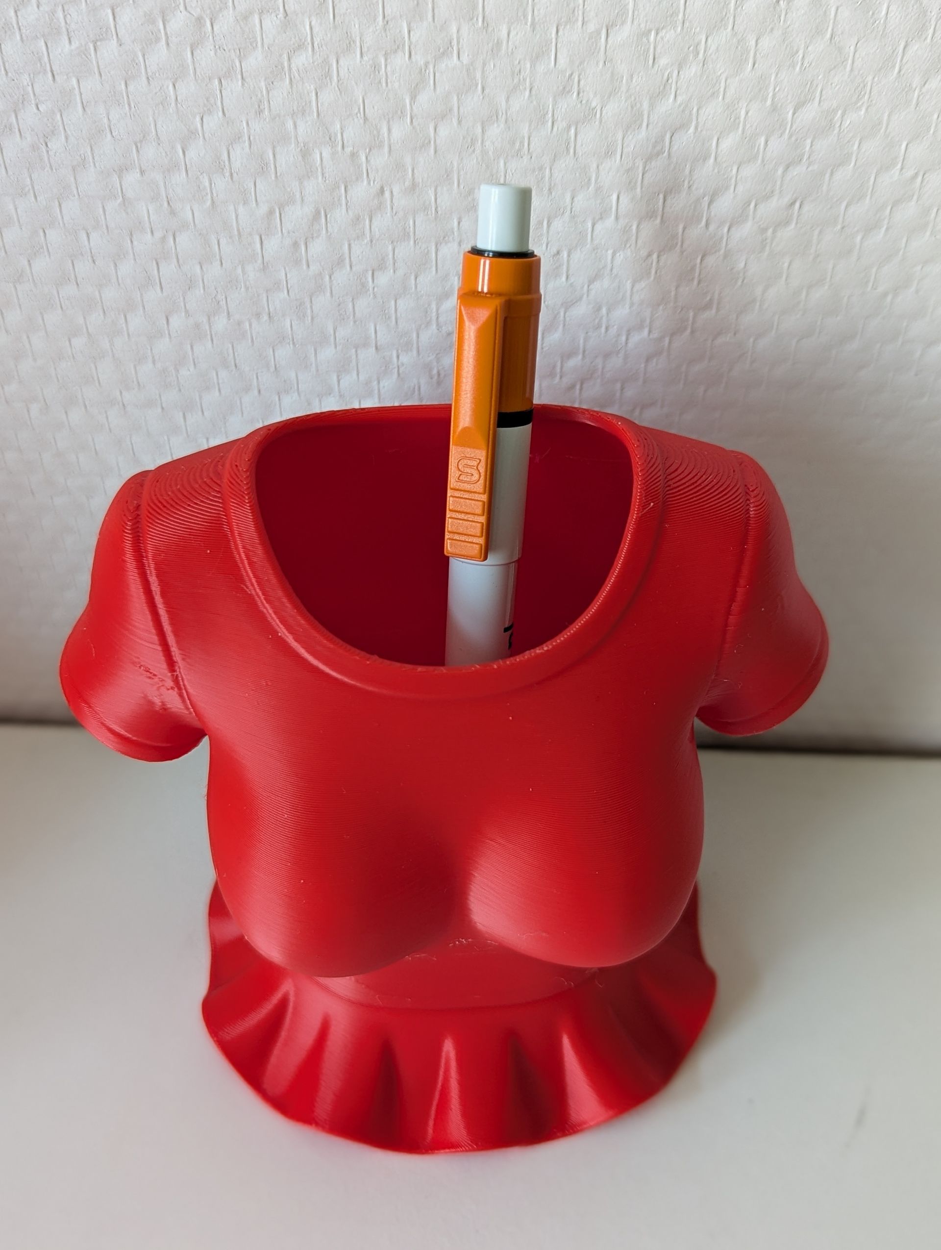 Rig-3d Een 3D-geprinte rode bureau-organizer in de vorm van een T-shirt met korte mouwen en een uitlopende zoom.