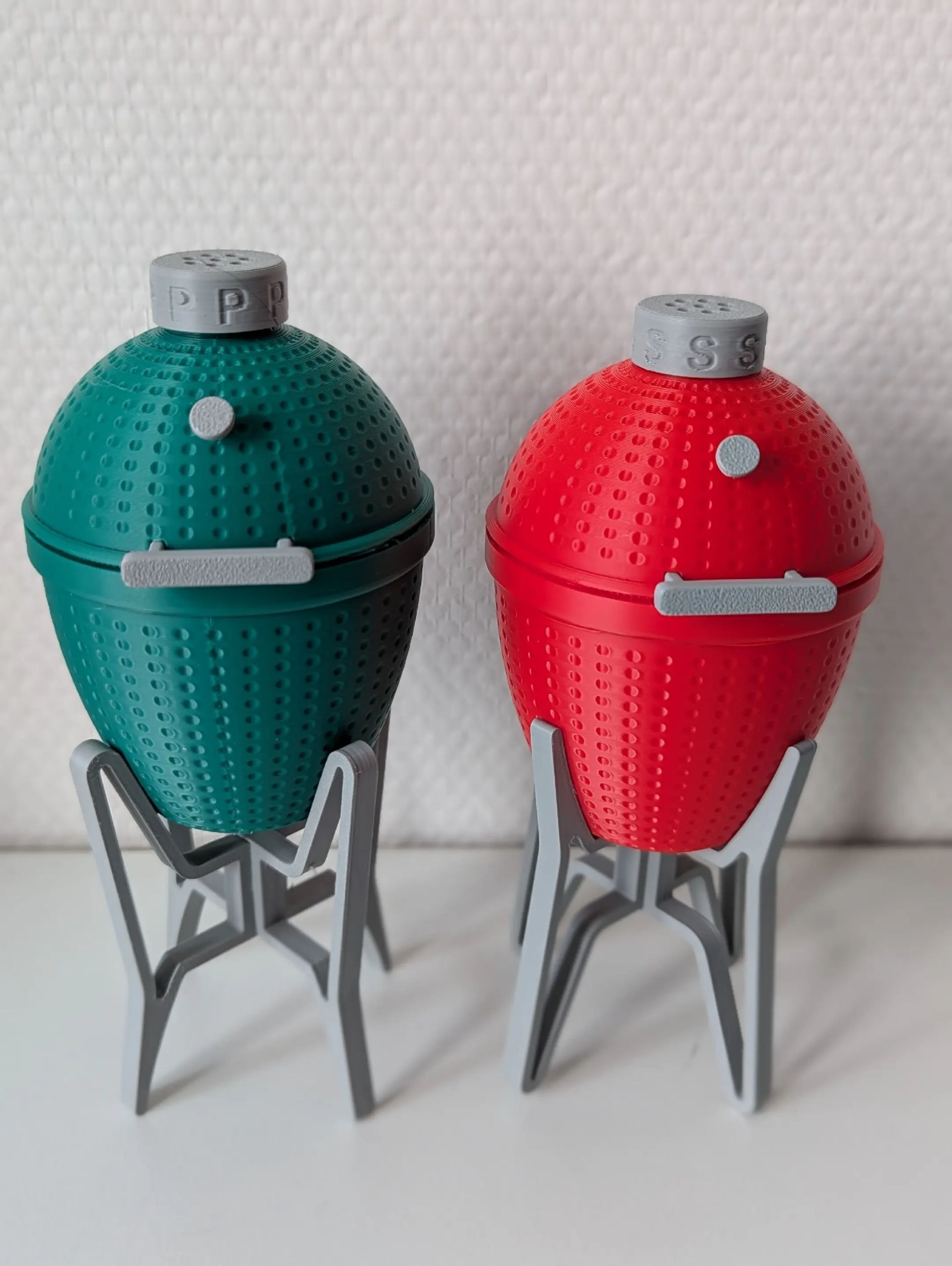 Rig-3d Een setje zout- en peperstrooiers in groen en rood, vormgegeven als mini-houtskoolgrills op grijze plastic voetjes.