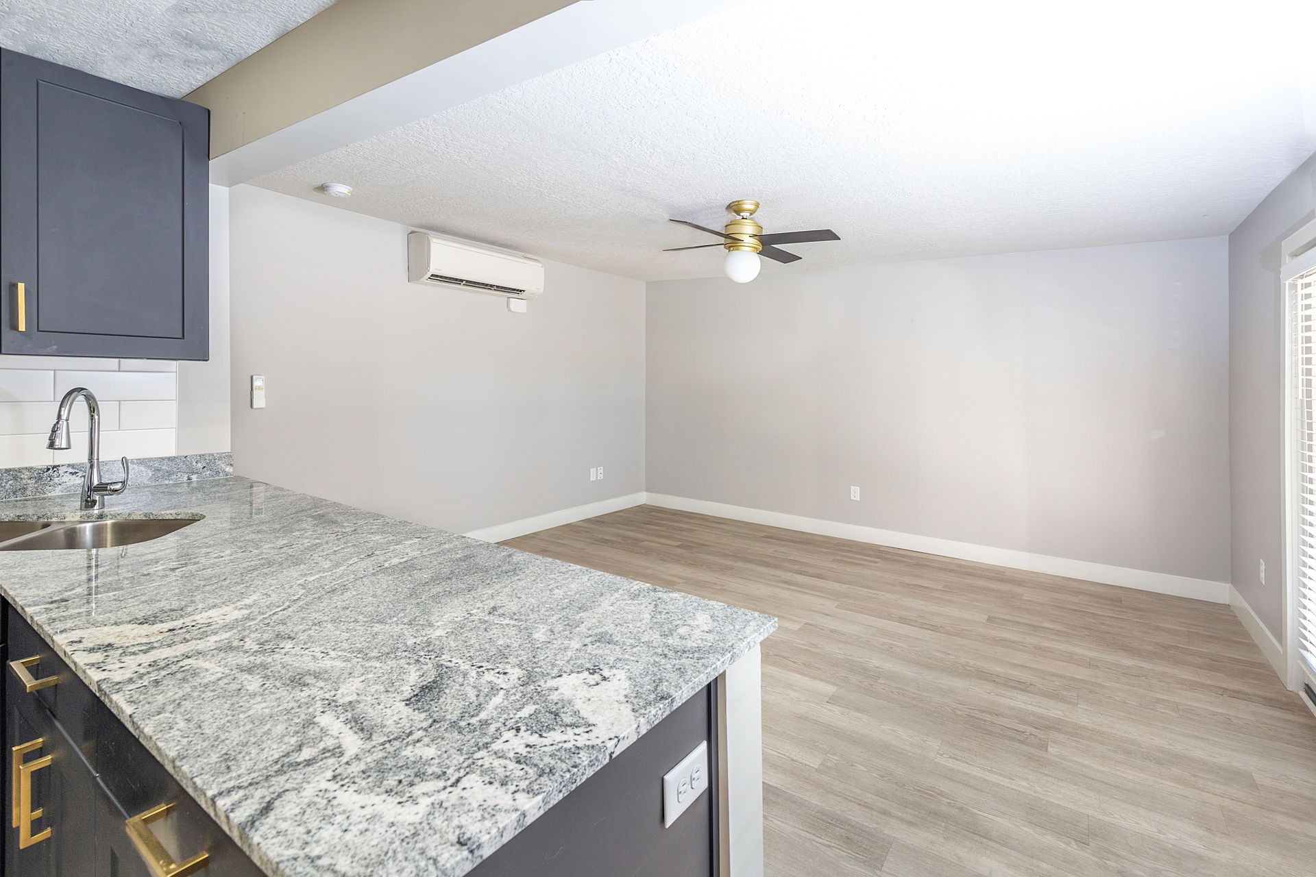 Kitchen and living area with gray cabinets, granite countertop, ceiling fan, and sliding glass door.