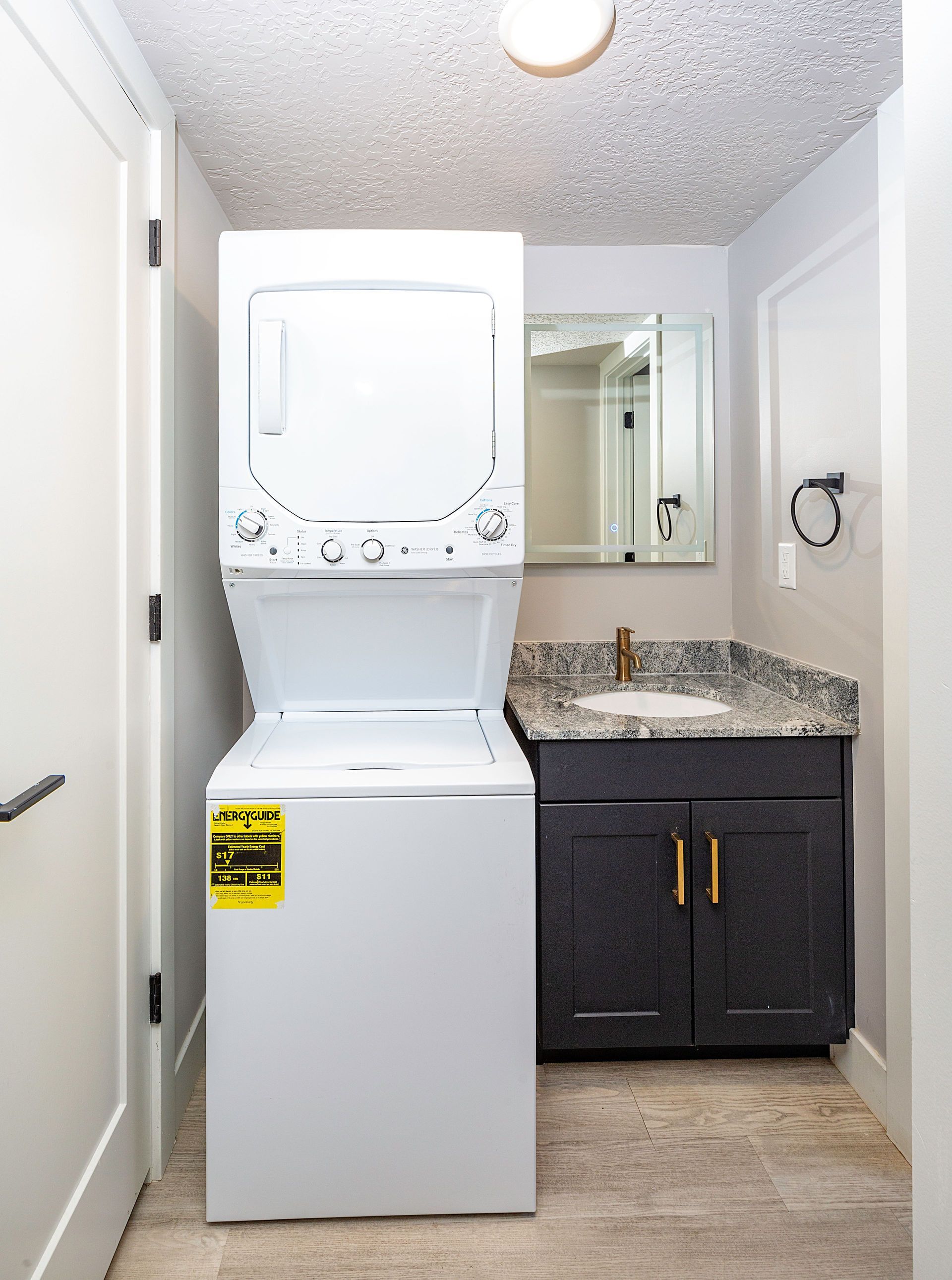 Stacked white washer and dryer next to a bathroom vanity with sink and mirror.