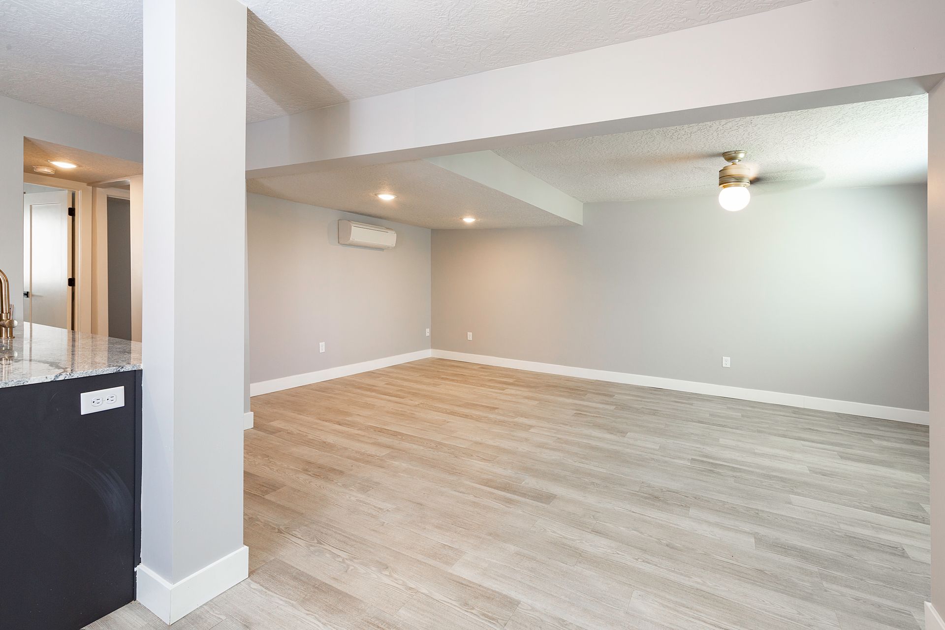 Empty basement room with light gray walls, wood-look flooring, and a ceiling fan.