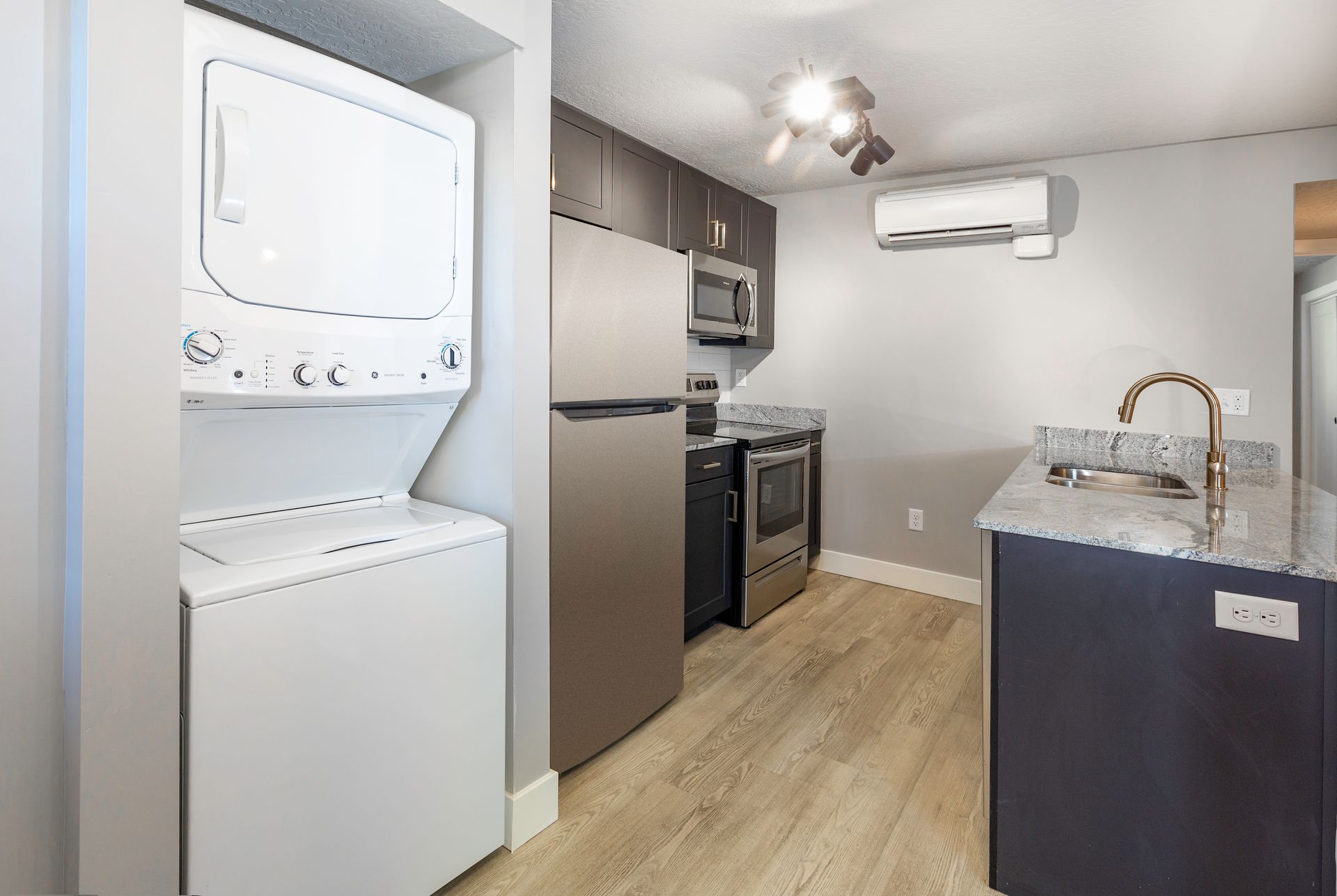 Small kitchen with stacked washer/dryer, stainless steel appliances, and a dark island with a sink.