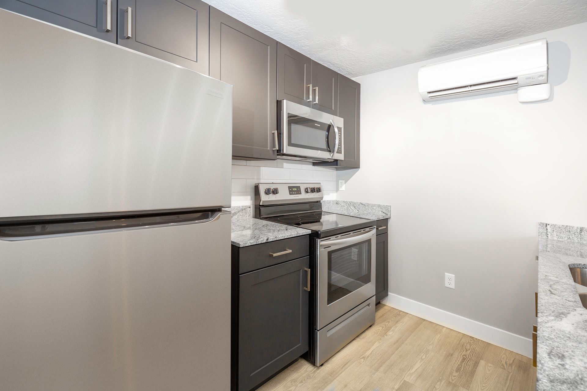 Modern kitchen with stainless steel appliances, dark cabinets, and light wood flooring.