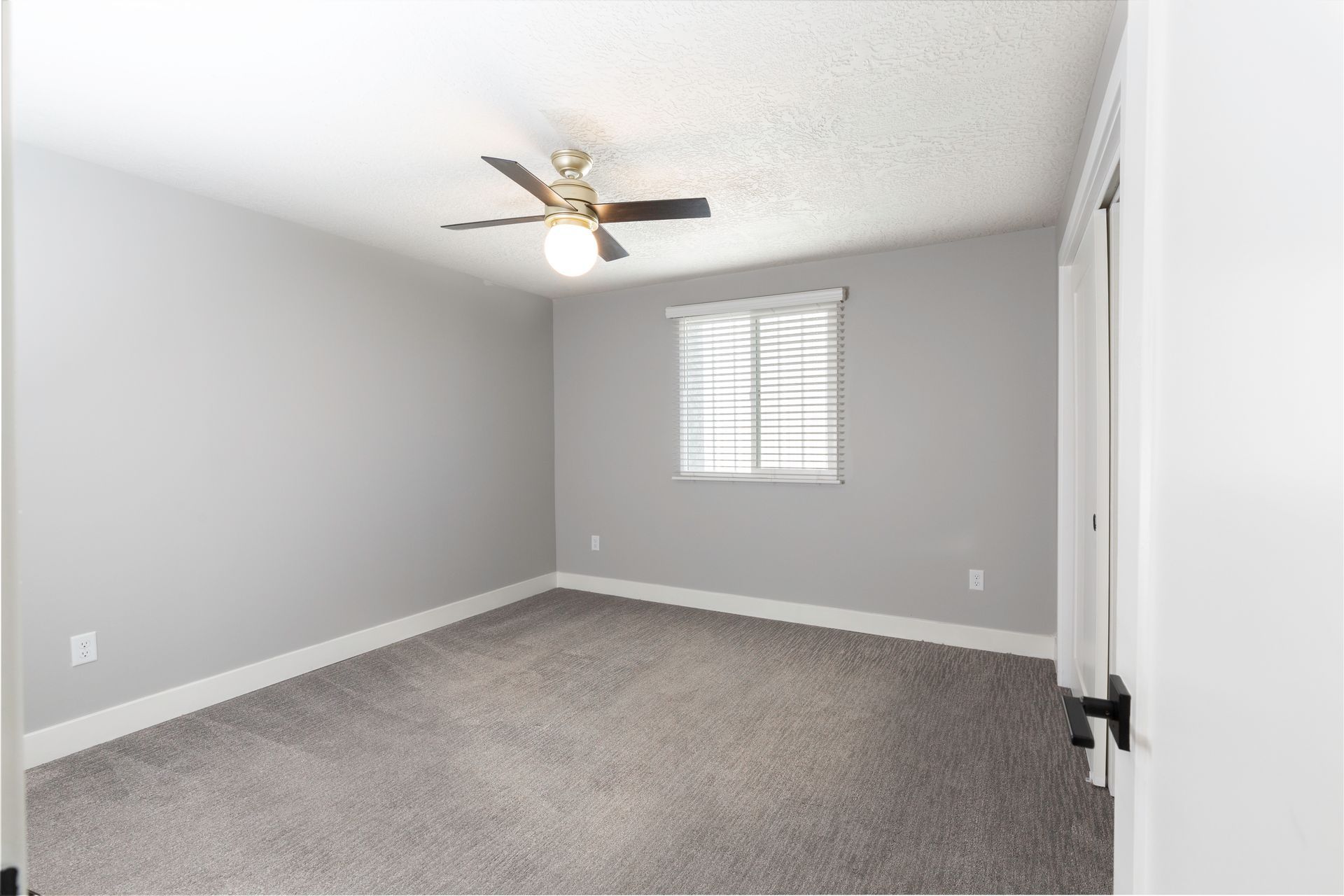 Empty bedroom with gray walls, carpet, and ceiling fan. Window with blinds.