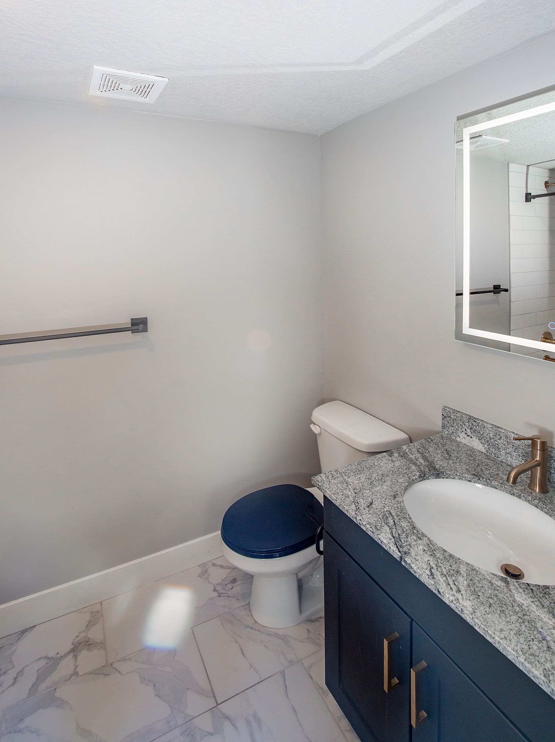 Modern bathroom with blue vanity, granite countertop, white toilet, and marble tile floor.