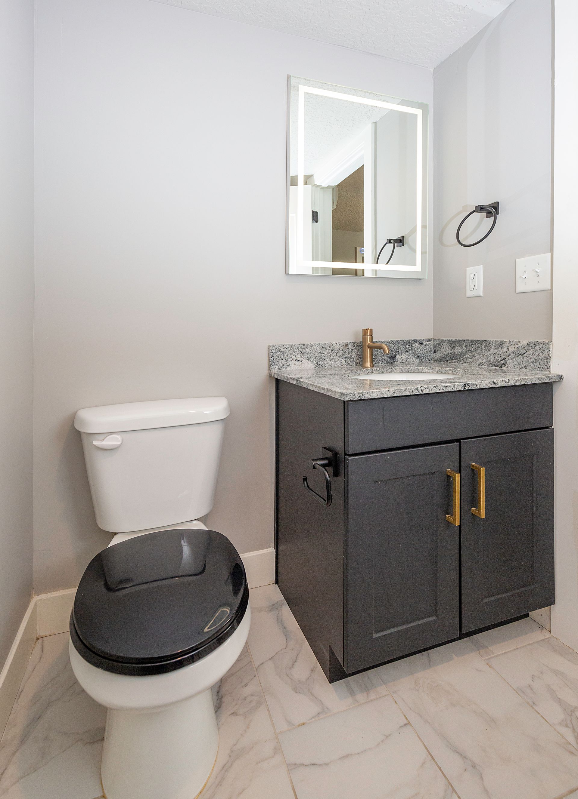 Bathroom with a gray vanity, granite countertop, lit mirror, and a toilet.