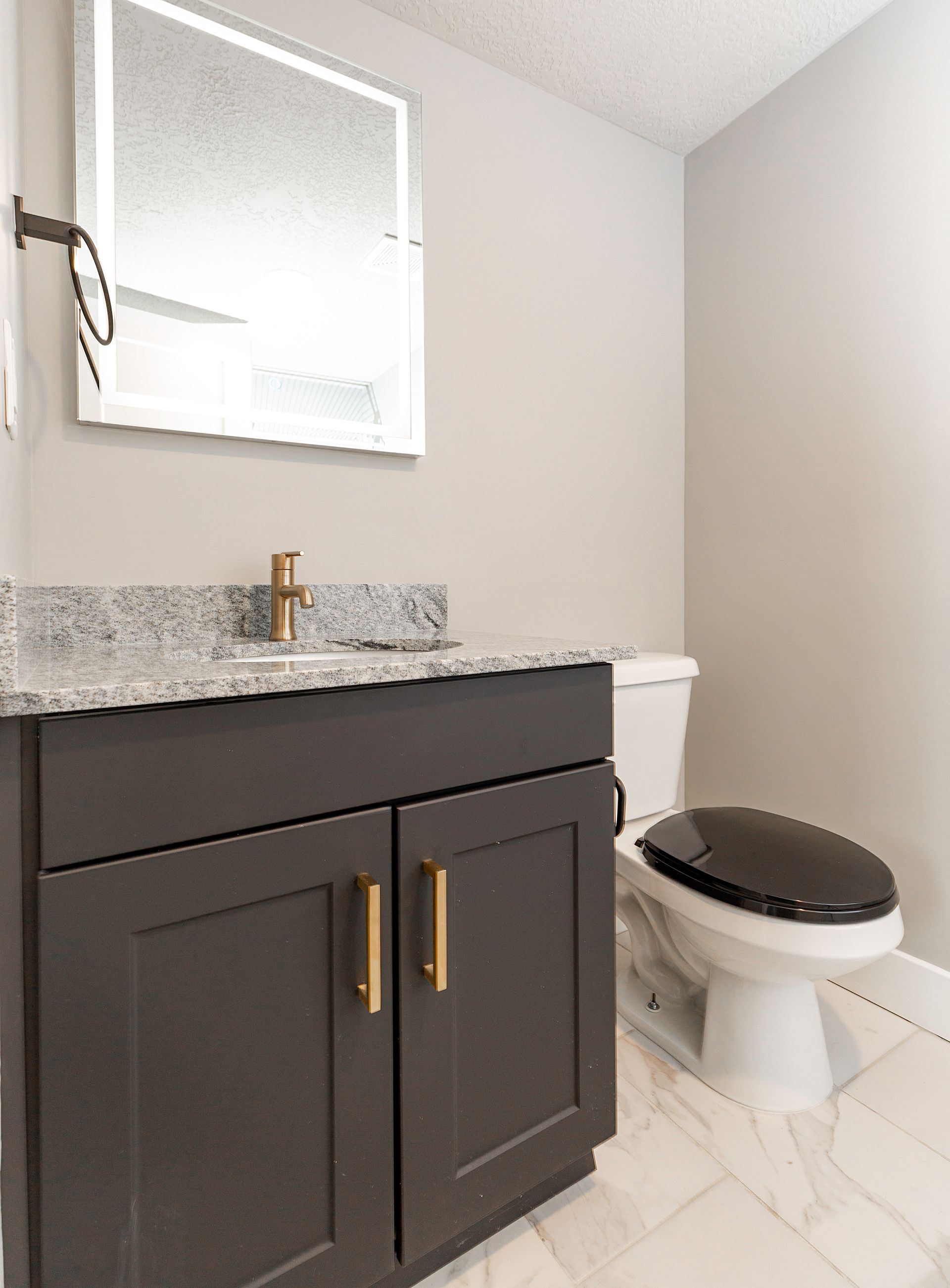 Bathroom with gray vanity, granite countertop, gold hardware, and a toilet.