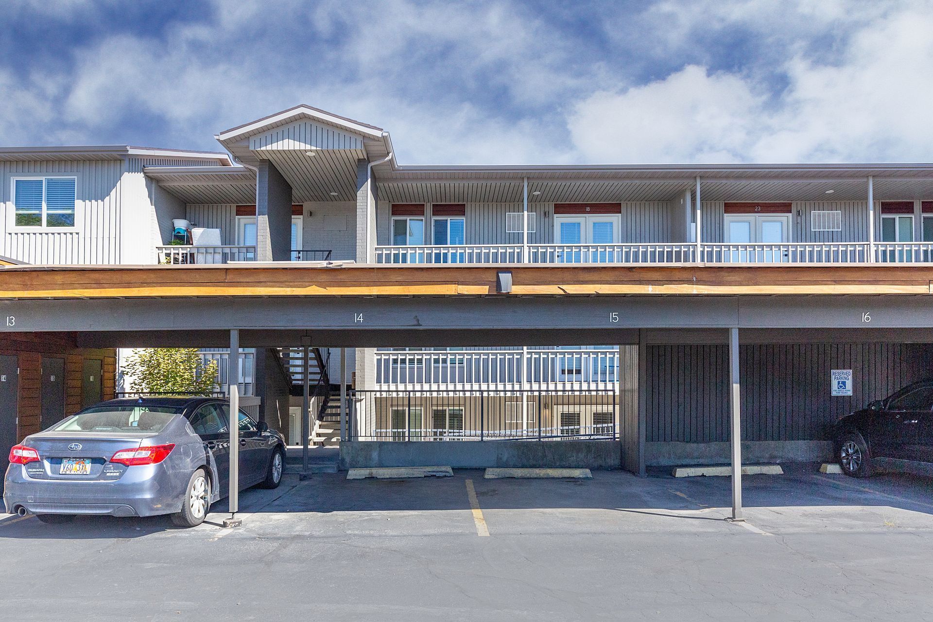 Apartment building with covered parking, gray exterior, cars parked underneath.