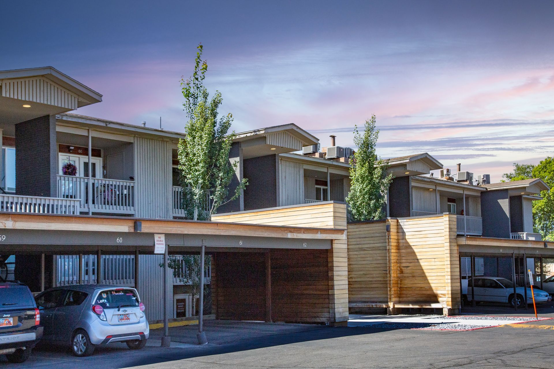 Townhouse exterior with covered parking, trees, and blue sky.