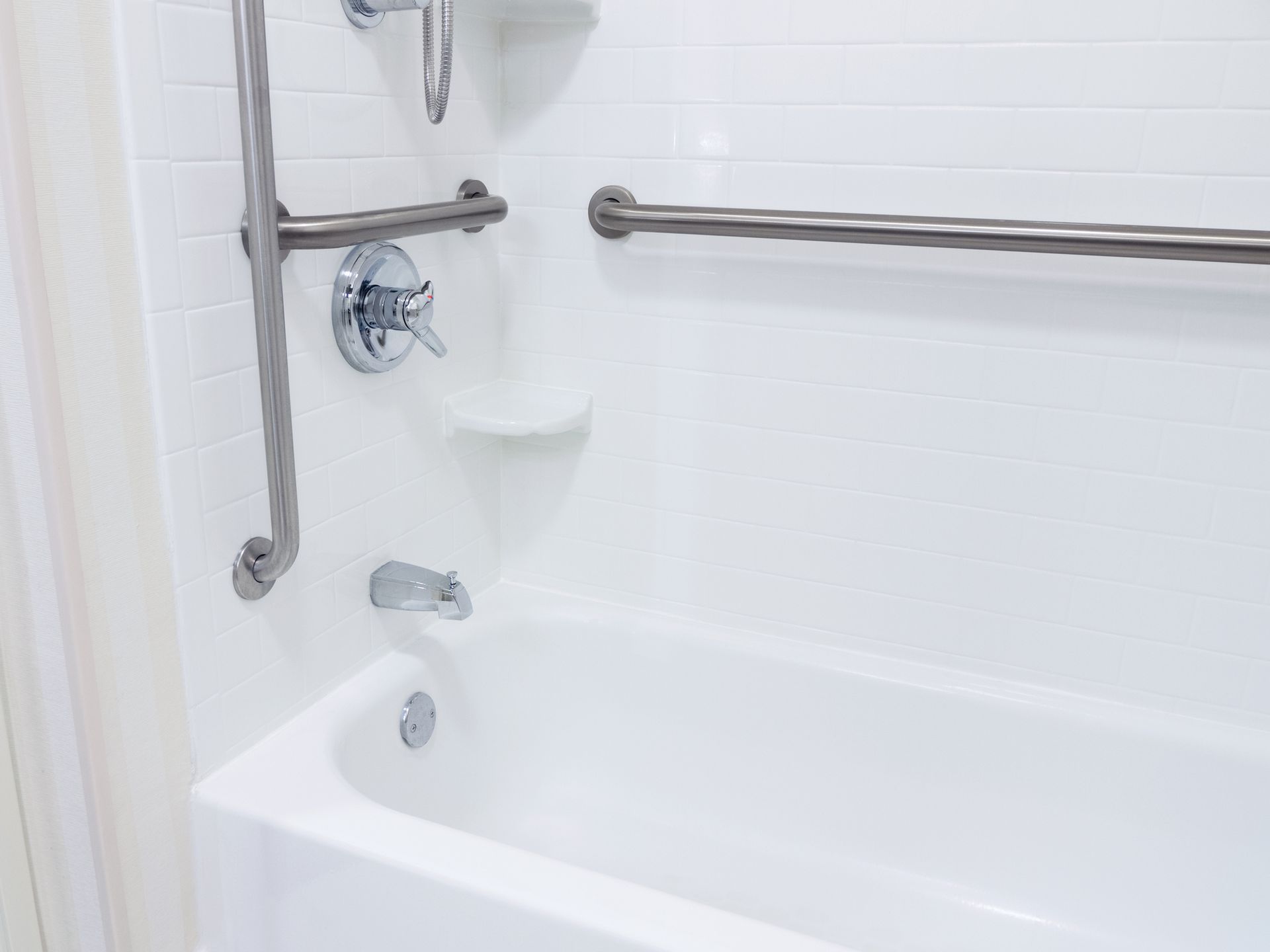 A white bathtub with stainless steel handles in a bathroom.