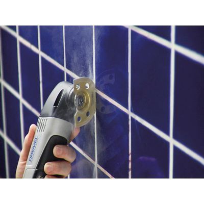 A person is using a multi tool to cut a hole in a tile wall.