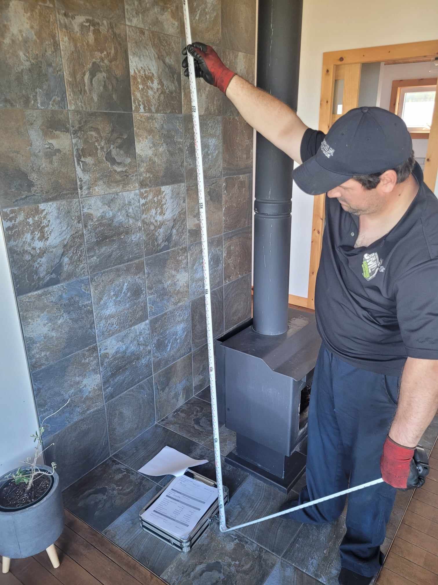 Un homme mesure une cheminée avec un ruban à mesurer dans un salon.