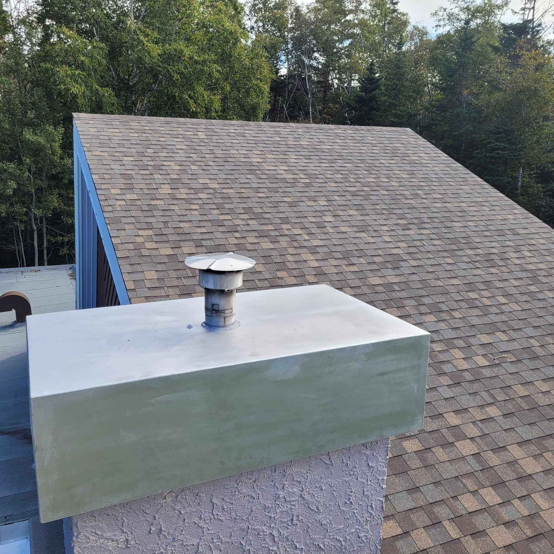 Une cheminée au sommet d'un toit avec des arbres en arrière-plan.