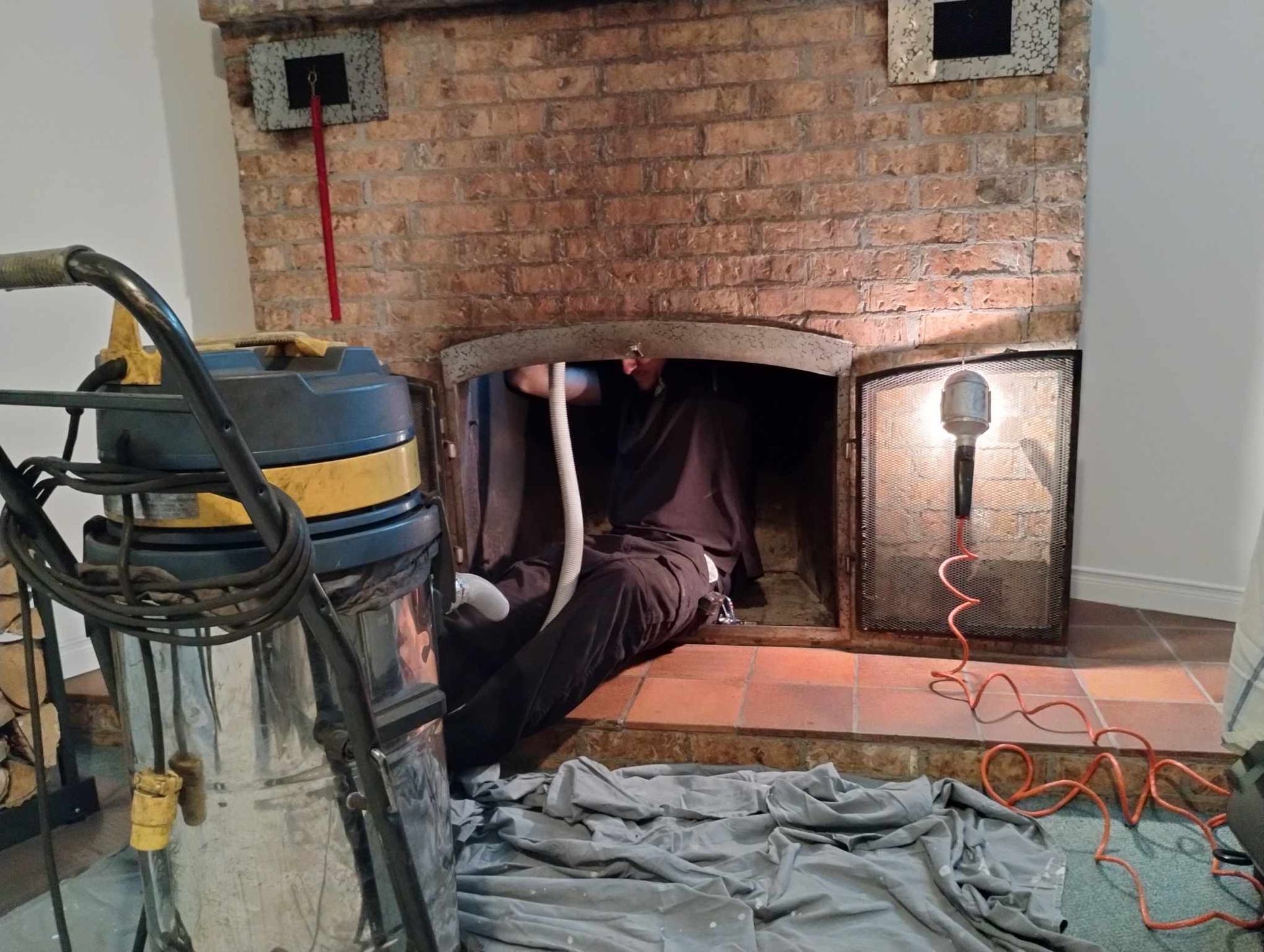 Un homme est assis dans une cheminée à côté d'un aspirateur.