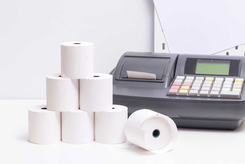 Rolls of paper are stacked on top of each other next to a cash register.