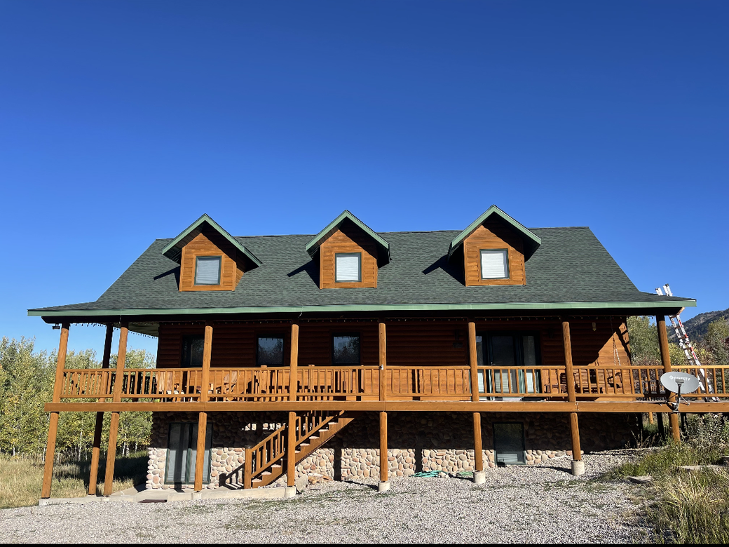 A large log cabin with a green roof and a large deck