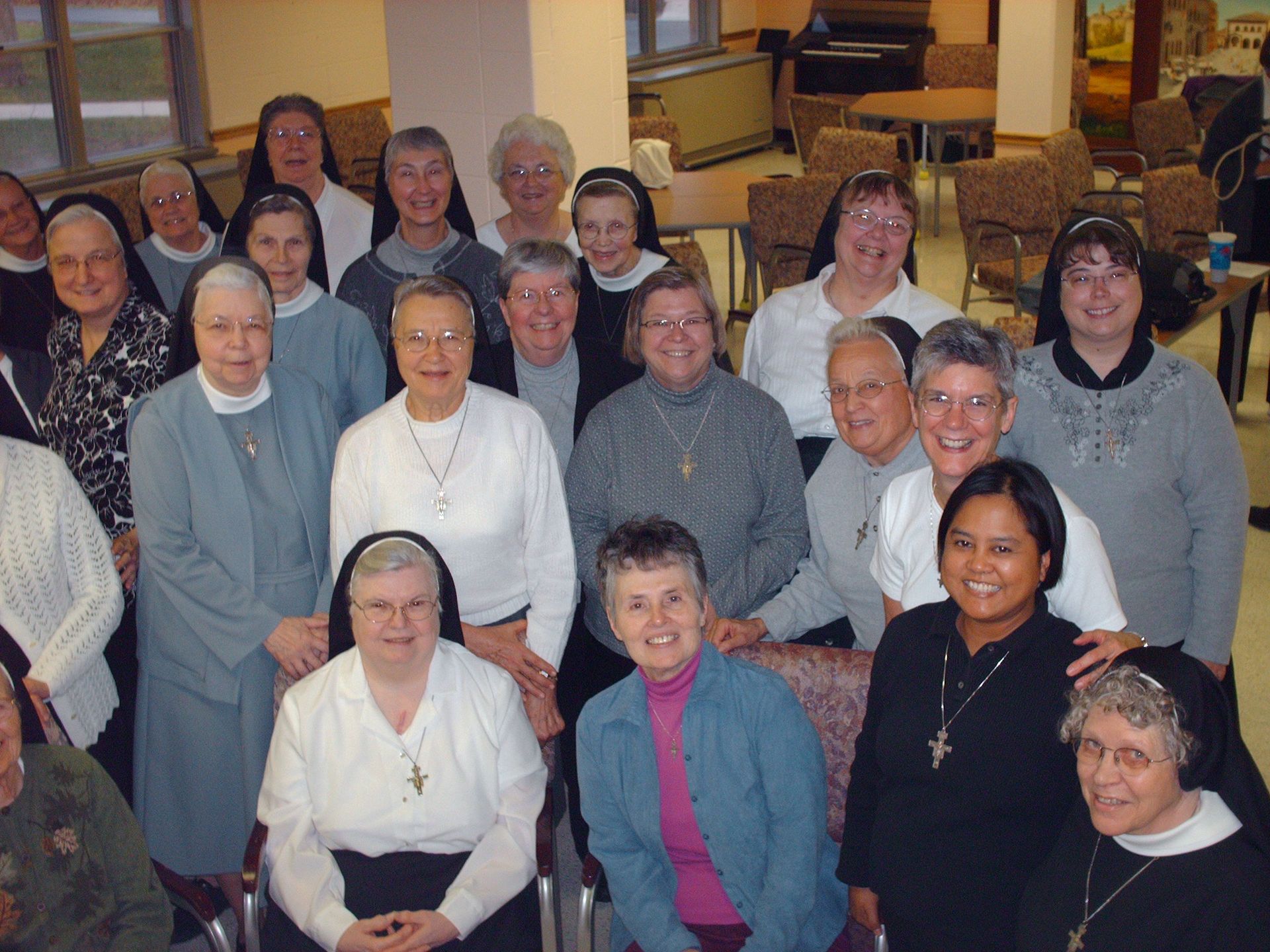 A large group of people in religious habits and civilian clothes posing for a photograph in an indoor common area.