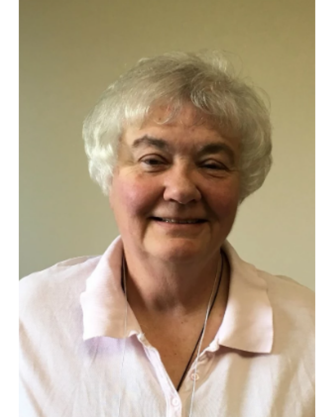 A person with light hair and a soft smile, wearing a pale pink collared shirt, against a plain light-colored background.