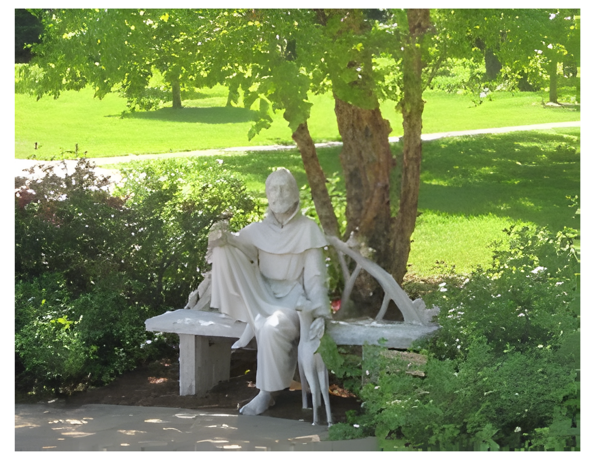 A white stone statue of a robed figure seated on a bench with a small animal, outdoors in a park setting.