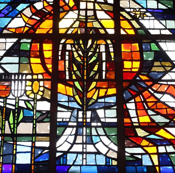 Stained glass window featuring a central golden cross and wheat stalk surrounded by vibrant red, orange, and blue panels.