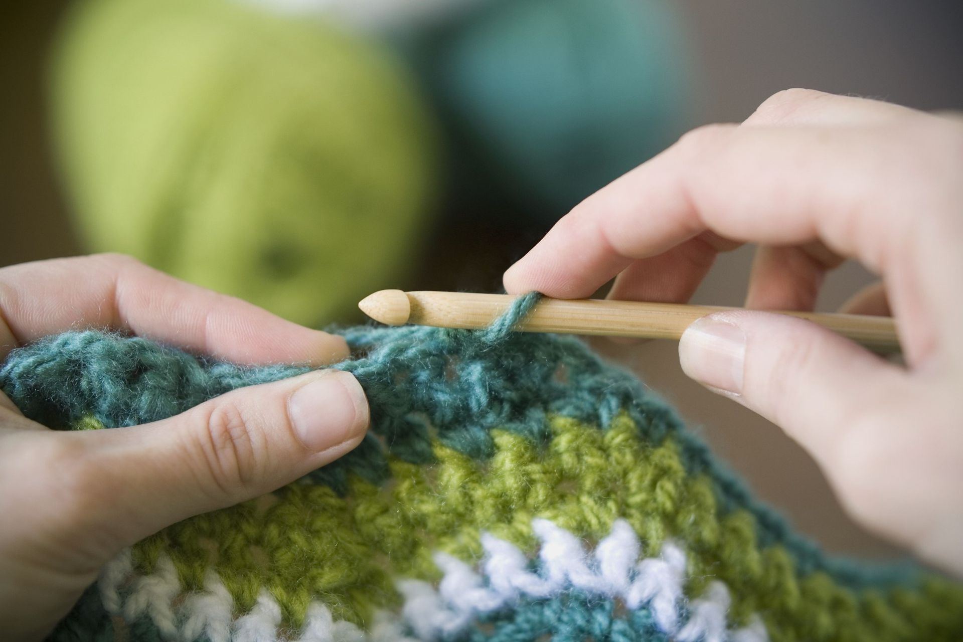 Close-up of hands using a bamboo crochet hook to work on a colorful, textured project with green and white yarn.