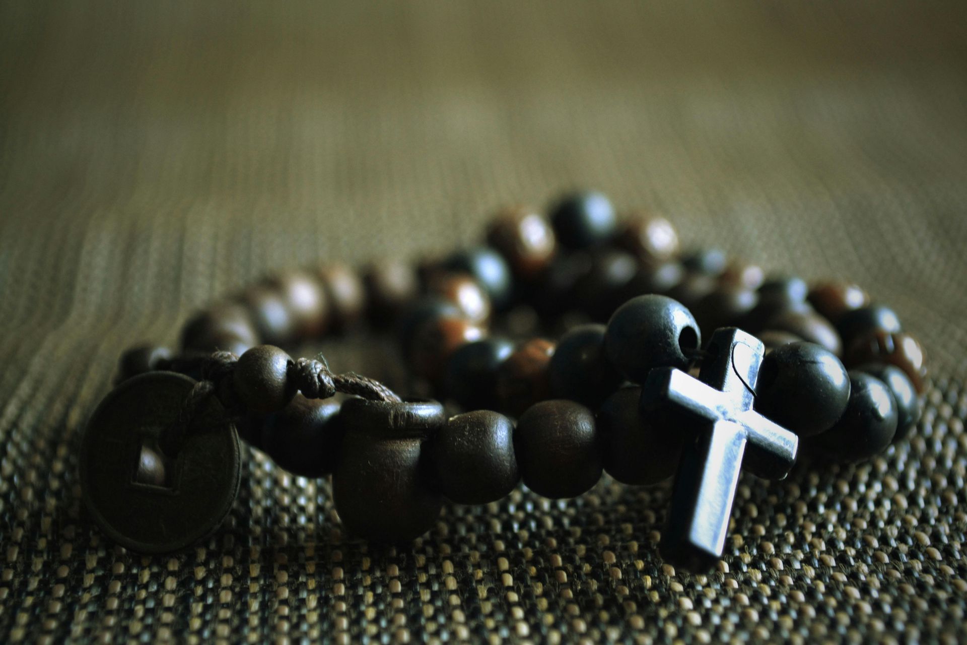 A close-up of dark wooden prayer beads arranged in a circular shape with a small cross attached on a textured surface.