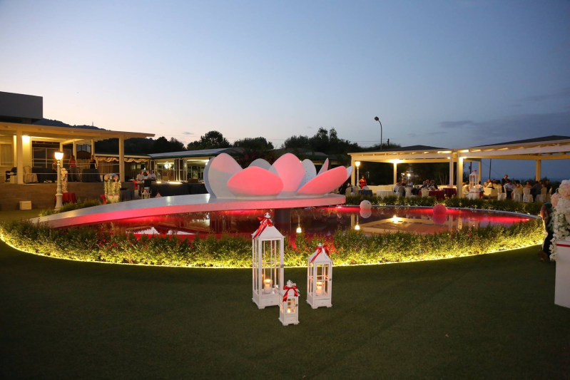 Fontana da giardino all'aperto illuminata di rosa al crepuscolo, con lanterne bianche e gli edifici del resort circostanti.