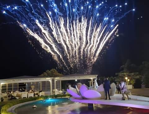 Un gruppo di persone in piedi davanti a una fontana che guarda i fuochi d'artificio.