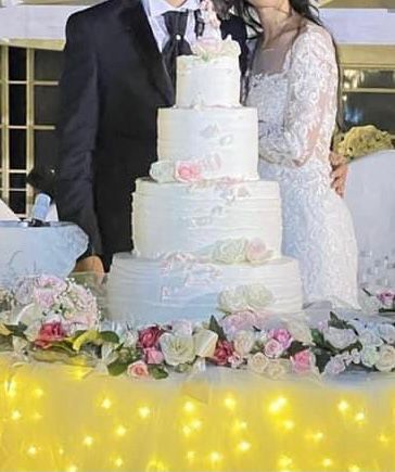 Gli sposi sono in piedi davanti a una torta nuziale.