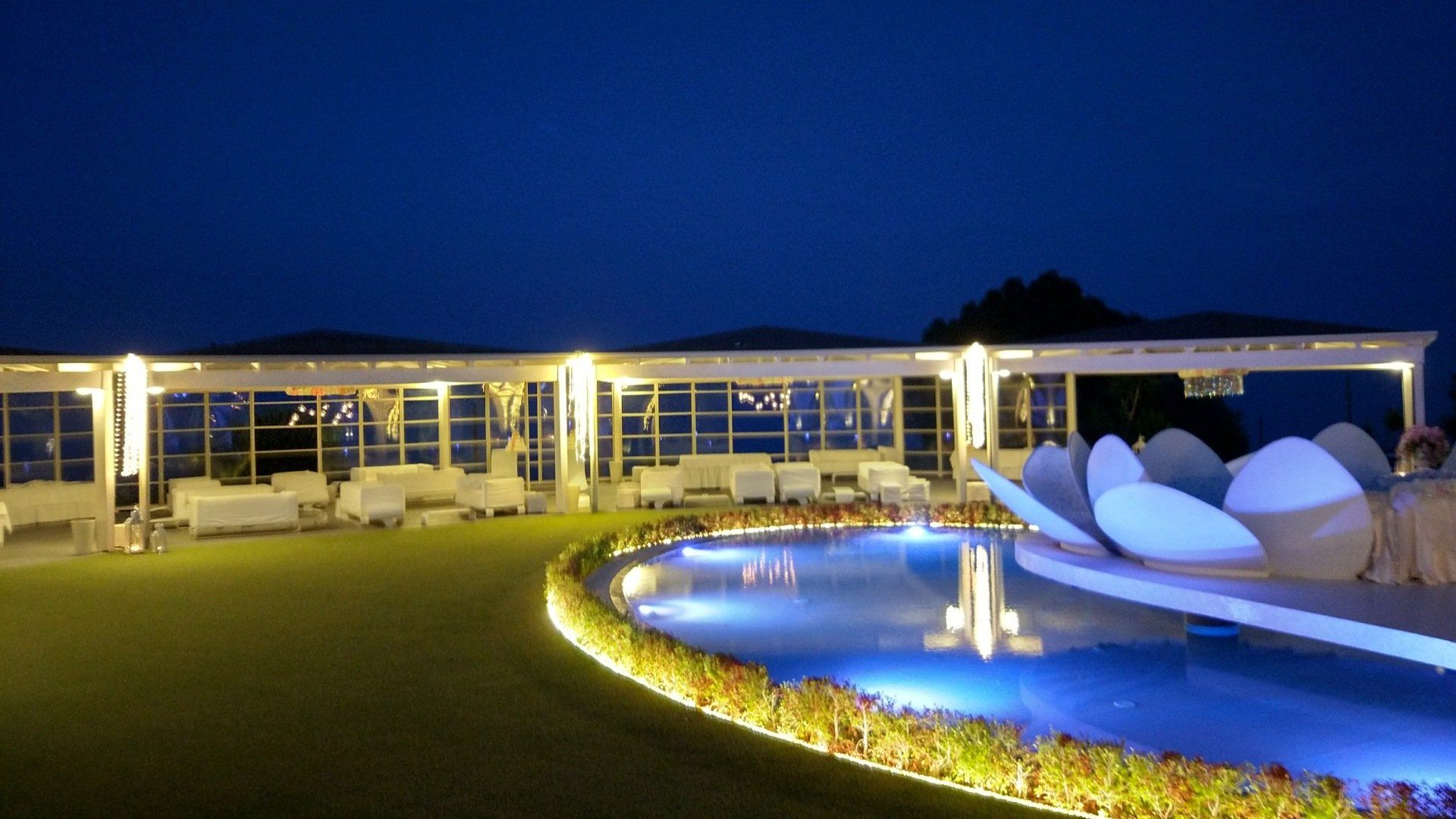 Un grande edificio bianco con una piscina di fronte di notte.